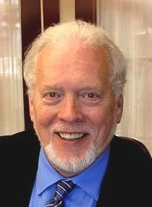 Tom Blaylock smiling in a blue shirt with white beard and hair.