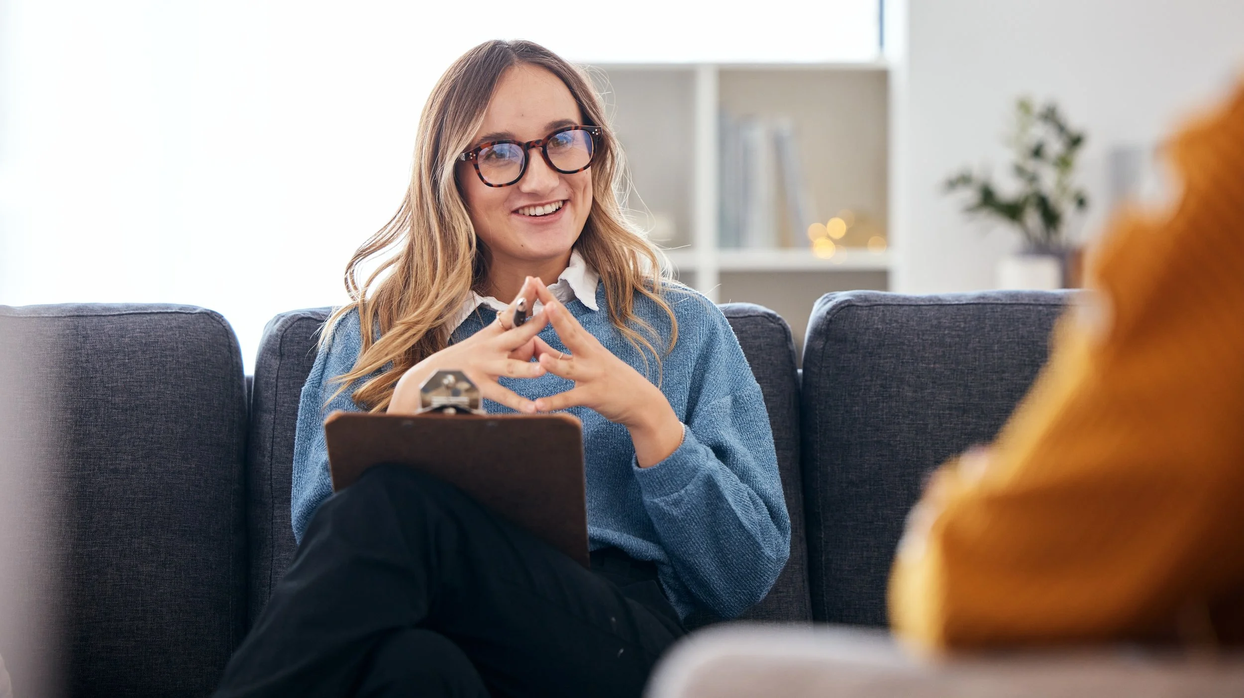 Therapist sitting on a couch with a relaxed posture, hands loosely clasped, talking with a client during an evidence-based, real-talk therapy session in Florida.
