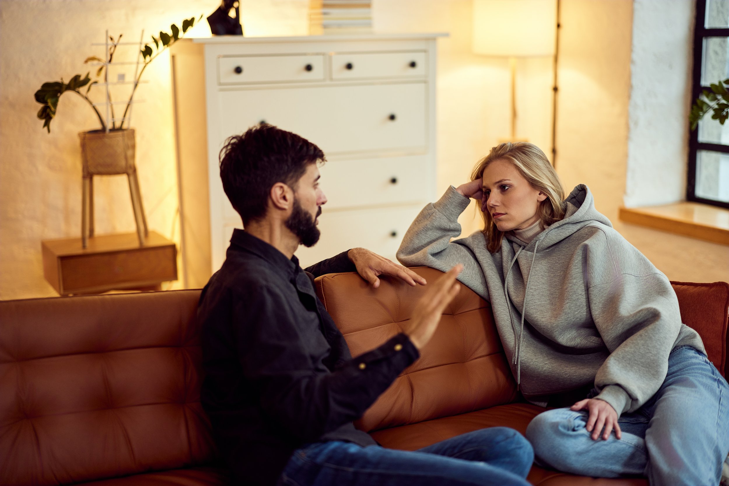 Couple in couples therapy style conversation on a couch, showing conflict and emotional regulation challenges