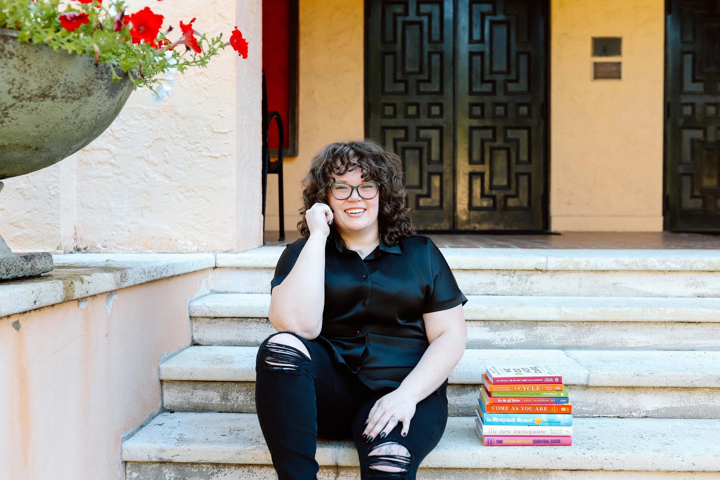 Therapist Mariah Plocinic sitting outdoors smiling beside relationship and women’s health books.
