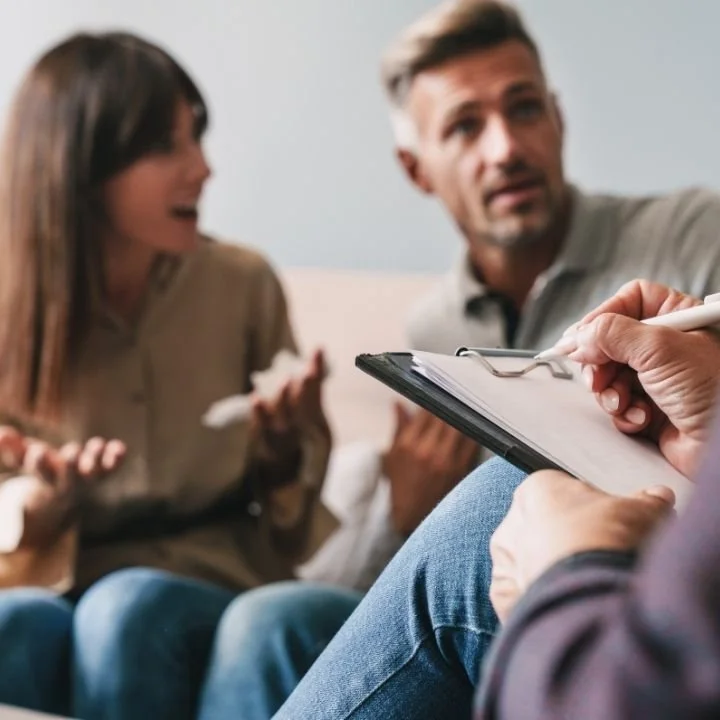 Therapist taking notes while helping a couple resolve relationship conflicts.