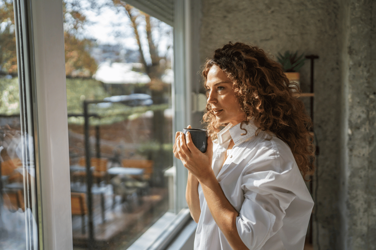 Woman holding a mug and reflecting by a window