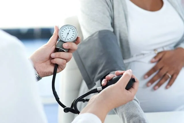 Healthcare professional measuring a pregnant woman's blood pressure with a sphygmomanometer.