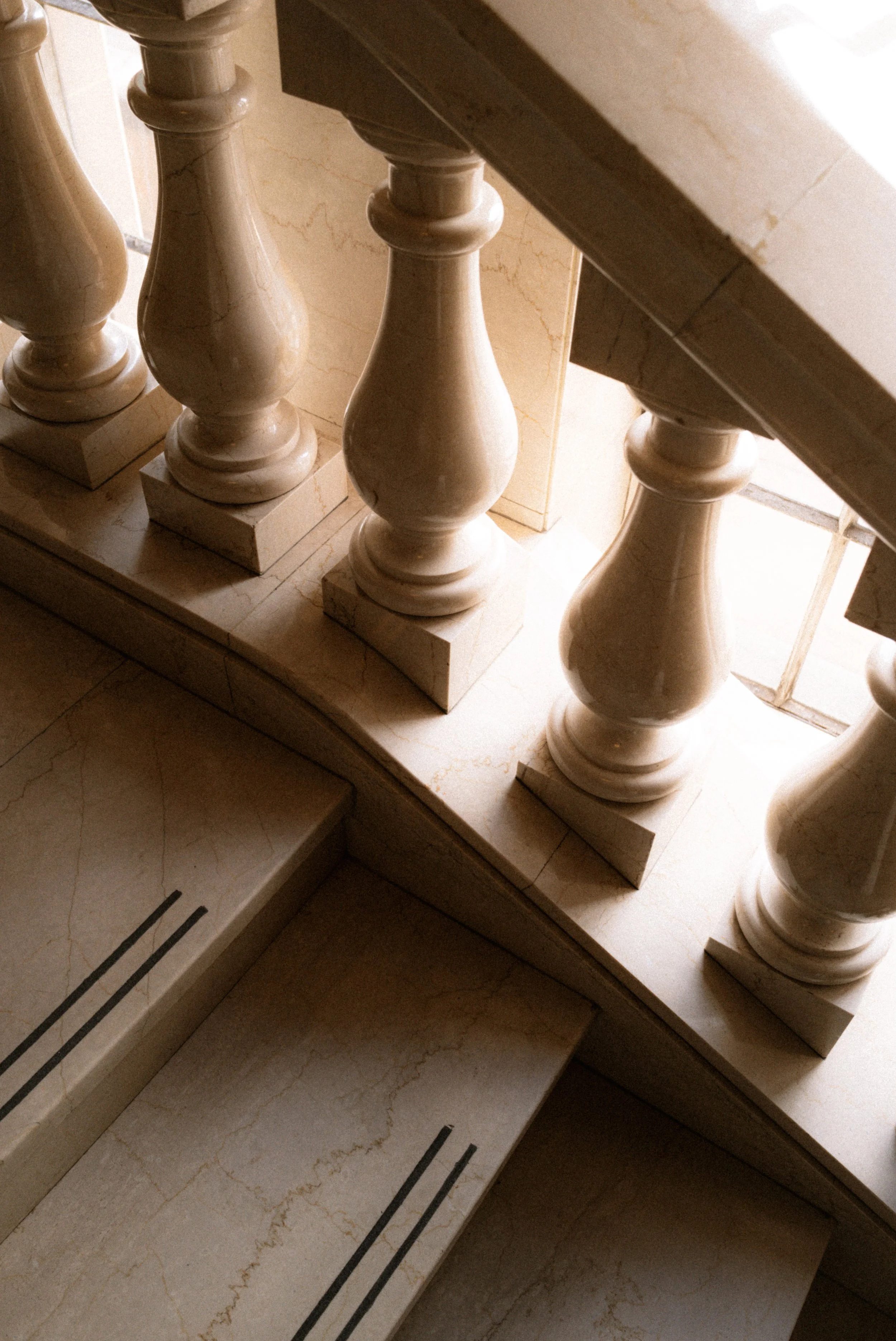 Close-up of a marble staircase with decorative balusters leading upwards, bathed in soft natural light.