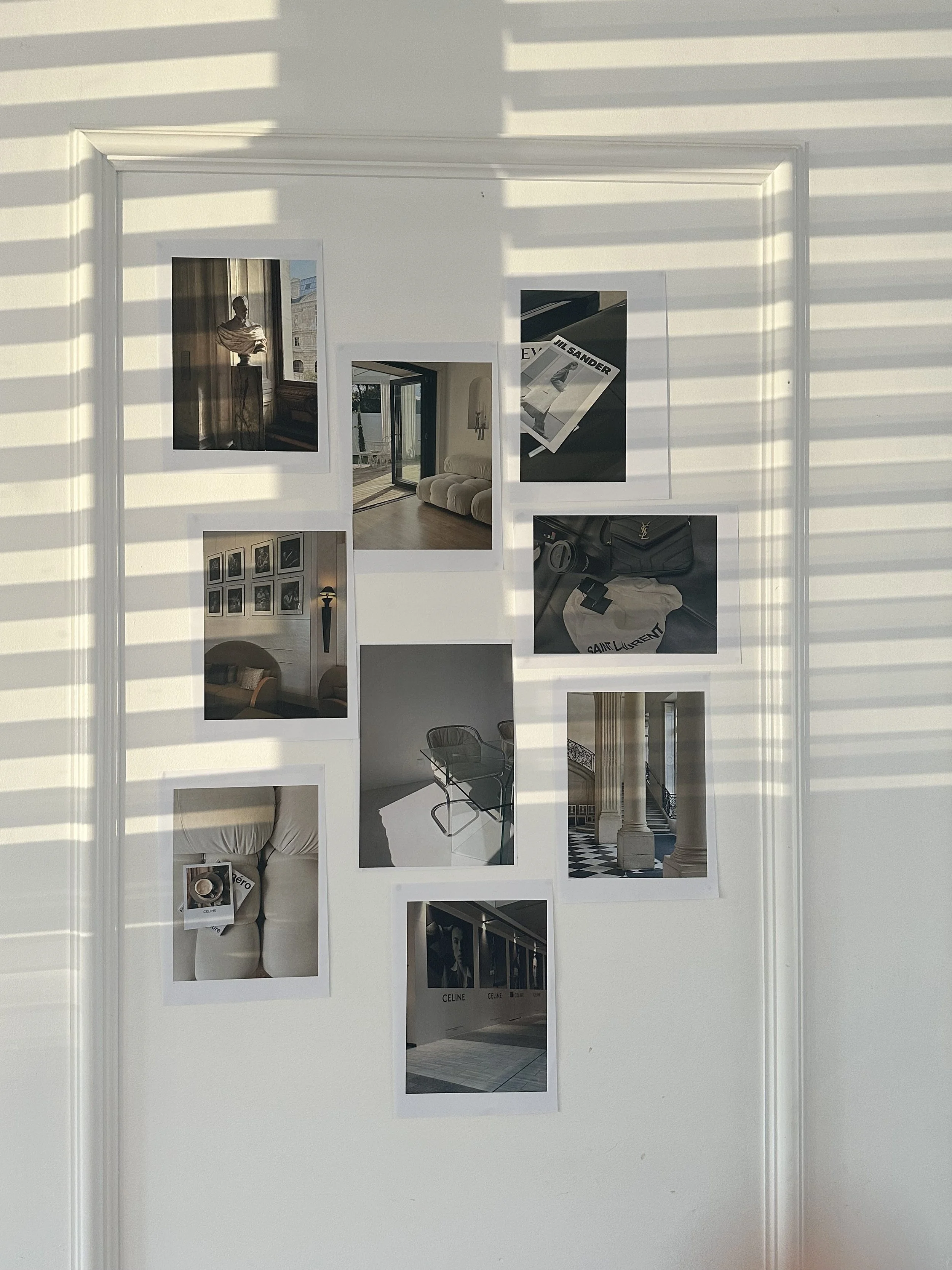Collection of nine photographs attached to a white wall, with sunlight and shadows creating horizontal lines across it. The photographs show interior and exterior scenes, fashion accessories, and artwork.