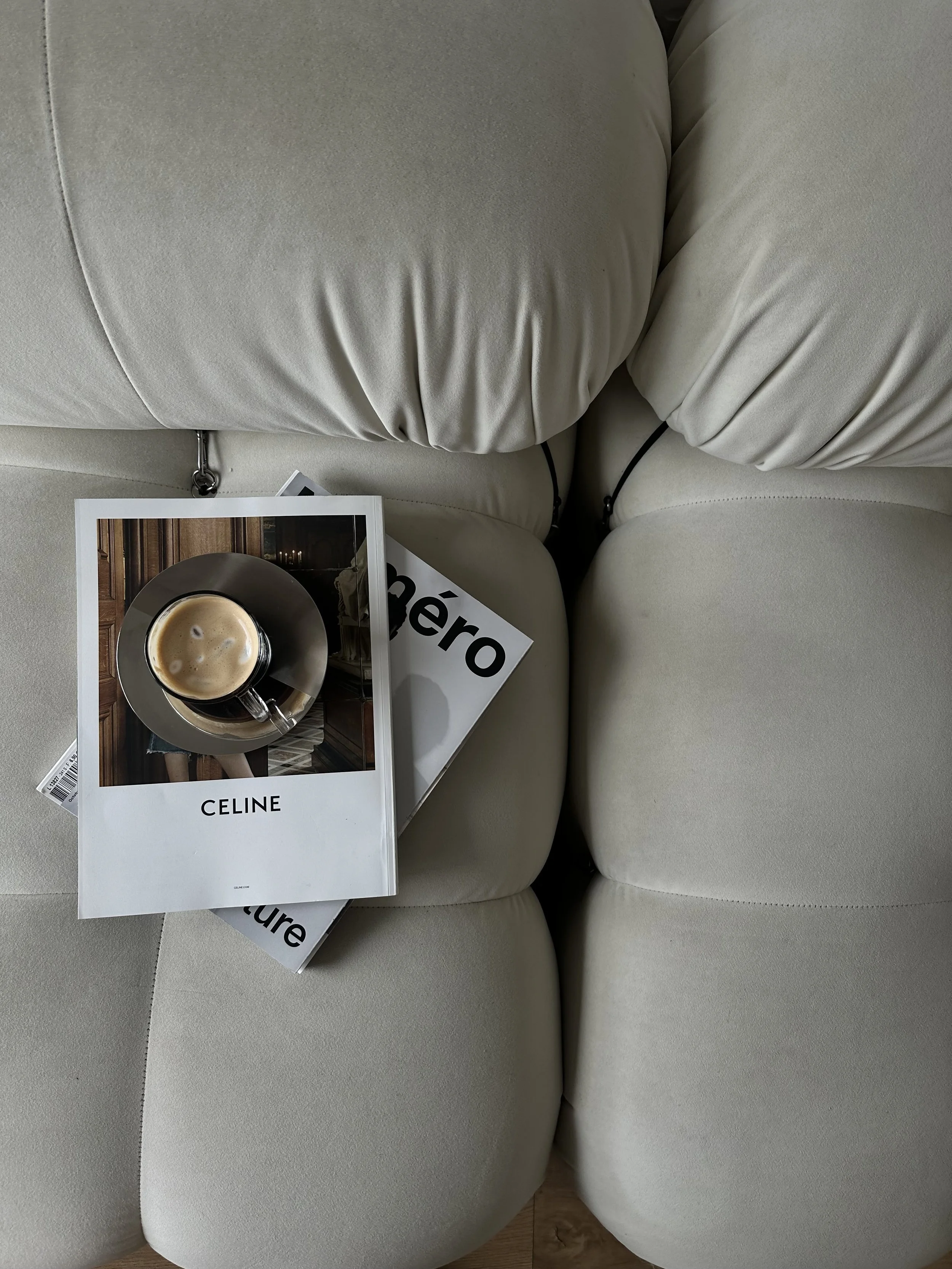 Top view of a white couch with a magazine, a book, and a coffee cup on it.