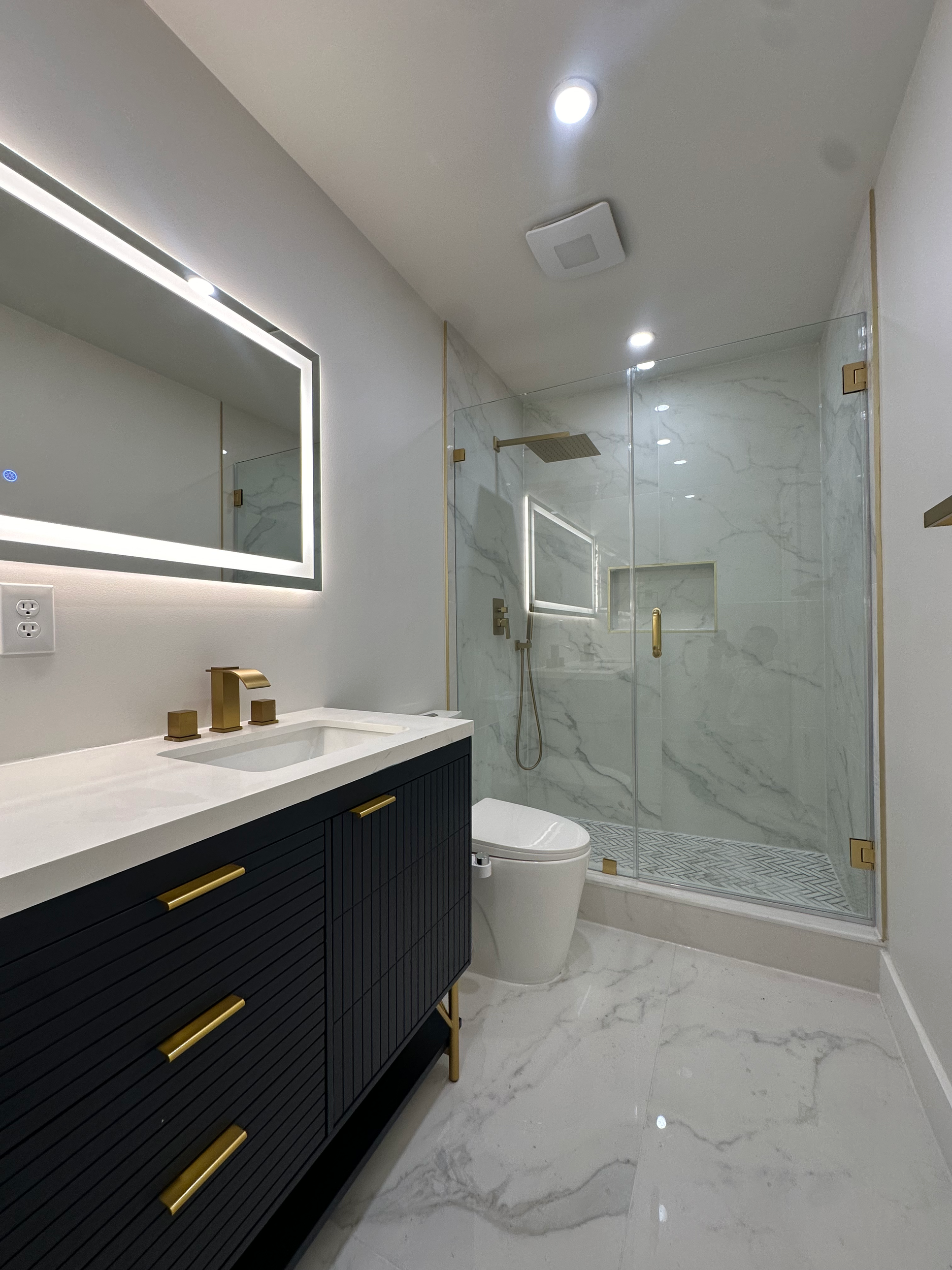 Modern bathroom with marble shower enclosure, black vanity with gold handles, and white toilet, illuminated by LED lighting and ceiling lights.