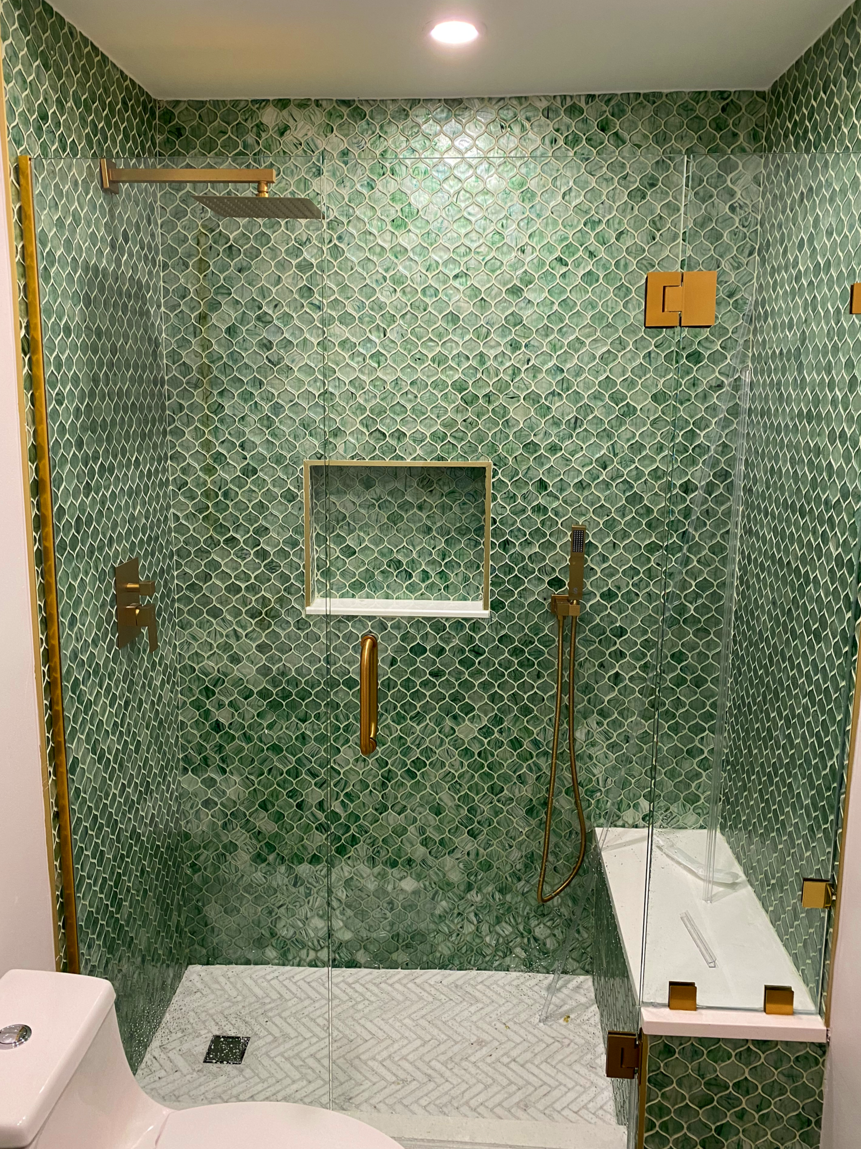Custom walk-in shower renovation completed in Alexandria, VA, featuring handcrafted green mosaic tile, frameless glass enclosure, integrated niche shelving, and brushed brass fixtures for a modern, spa-like finish.