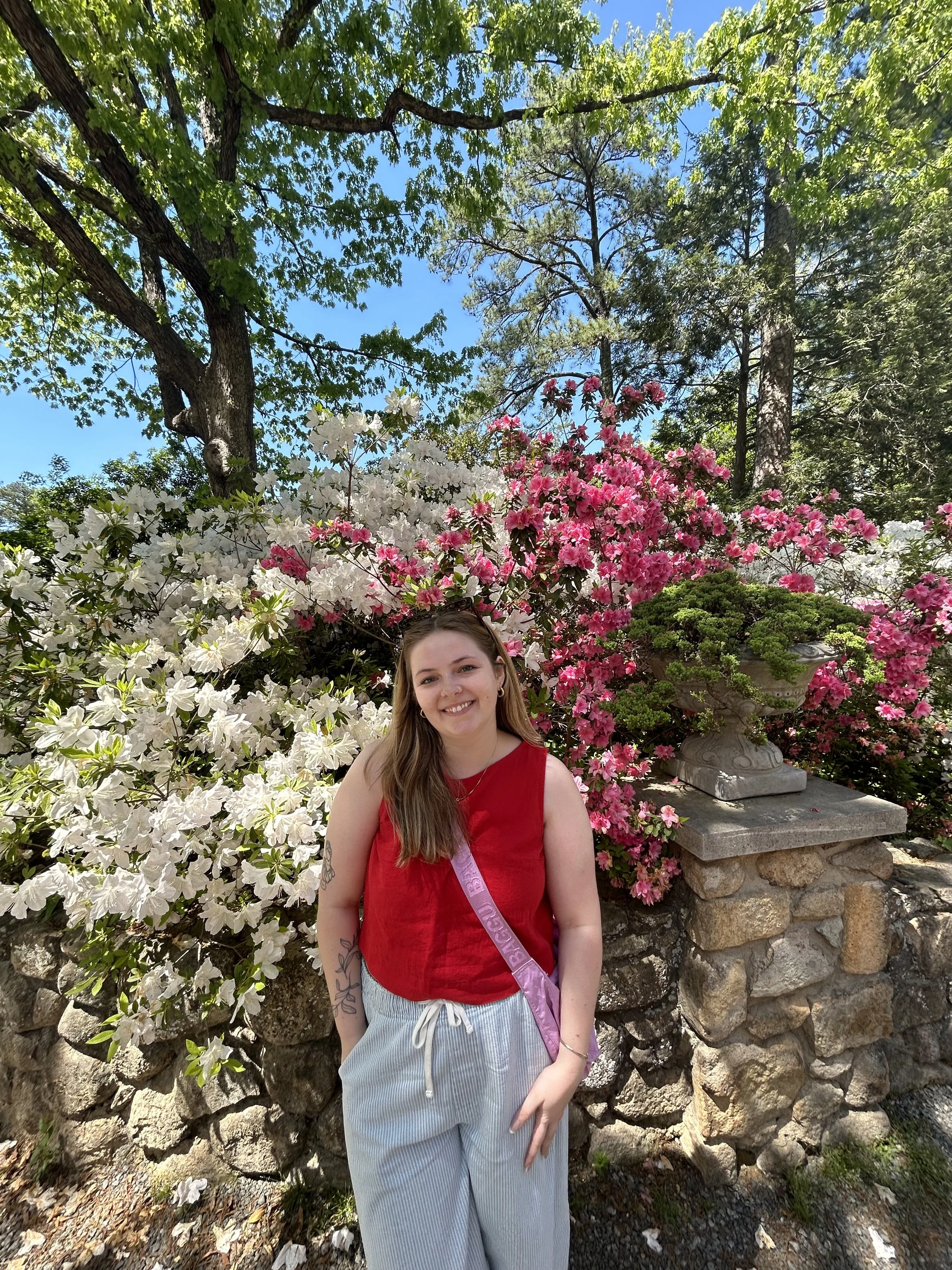 An individual is smiling in front of a vibrant flower bush.