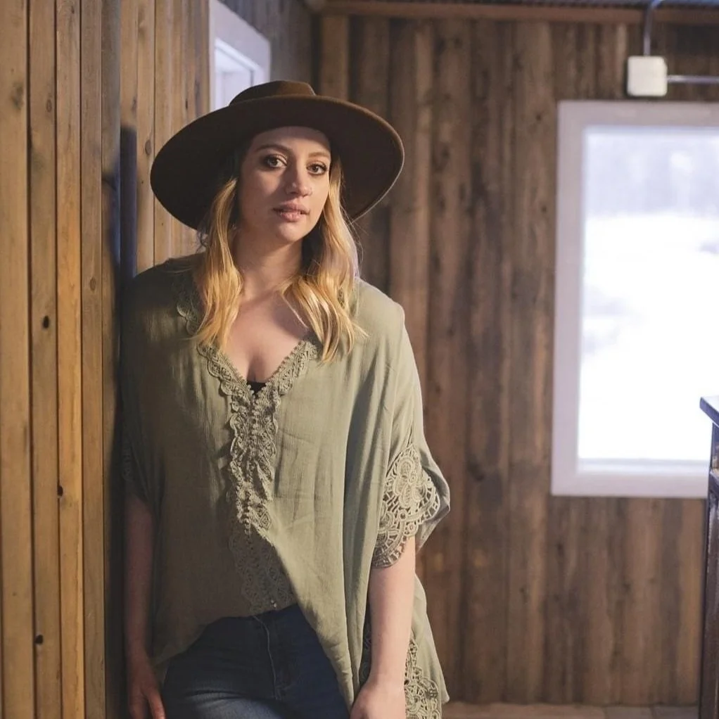 A portrait of a individual wearing a hat, set against a background of wooden panel walls and a window.
