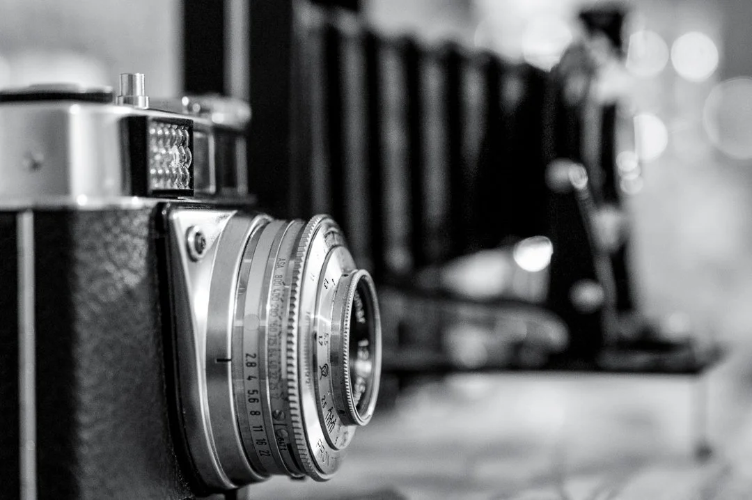 Close-up of a vintage camera with a textured body, focus on the lens, in black and white.