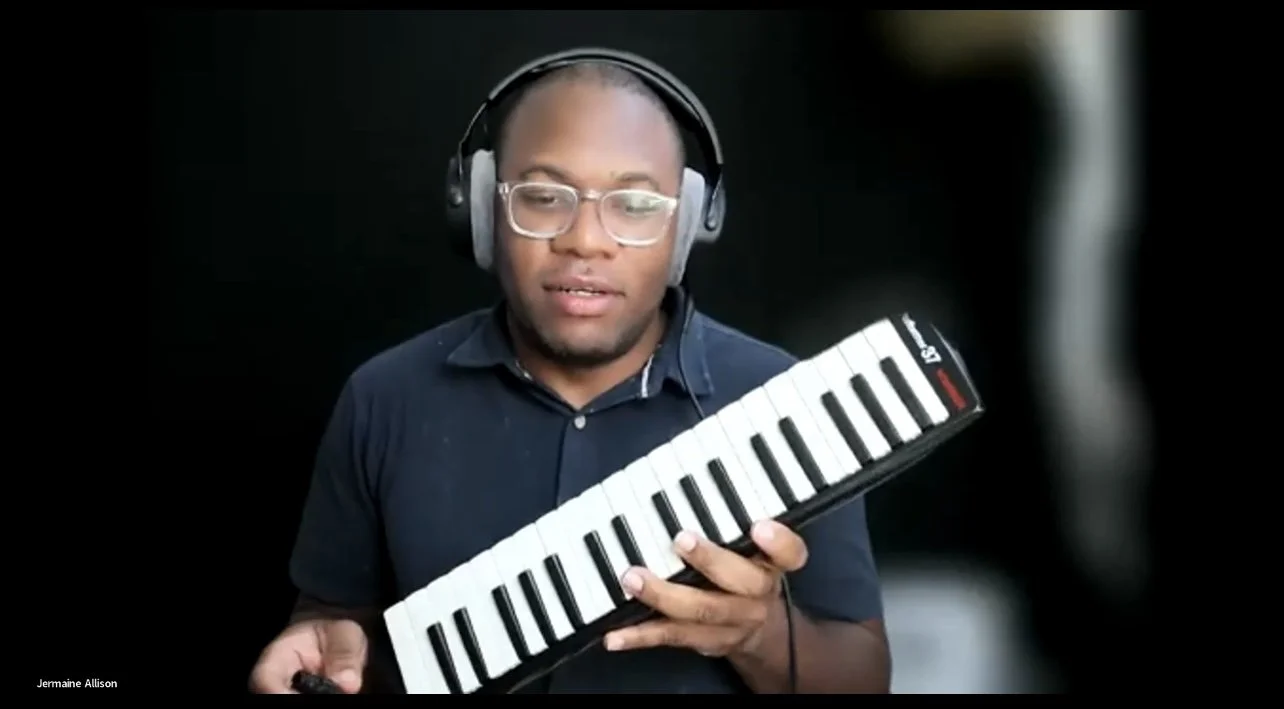 A man wearing glasses and headphones is playing a portable electronic keyboard against a black background.