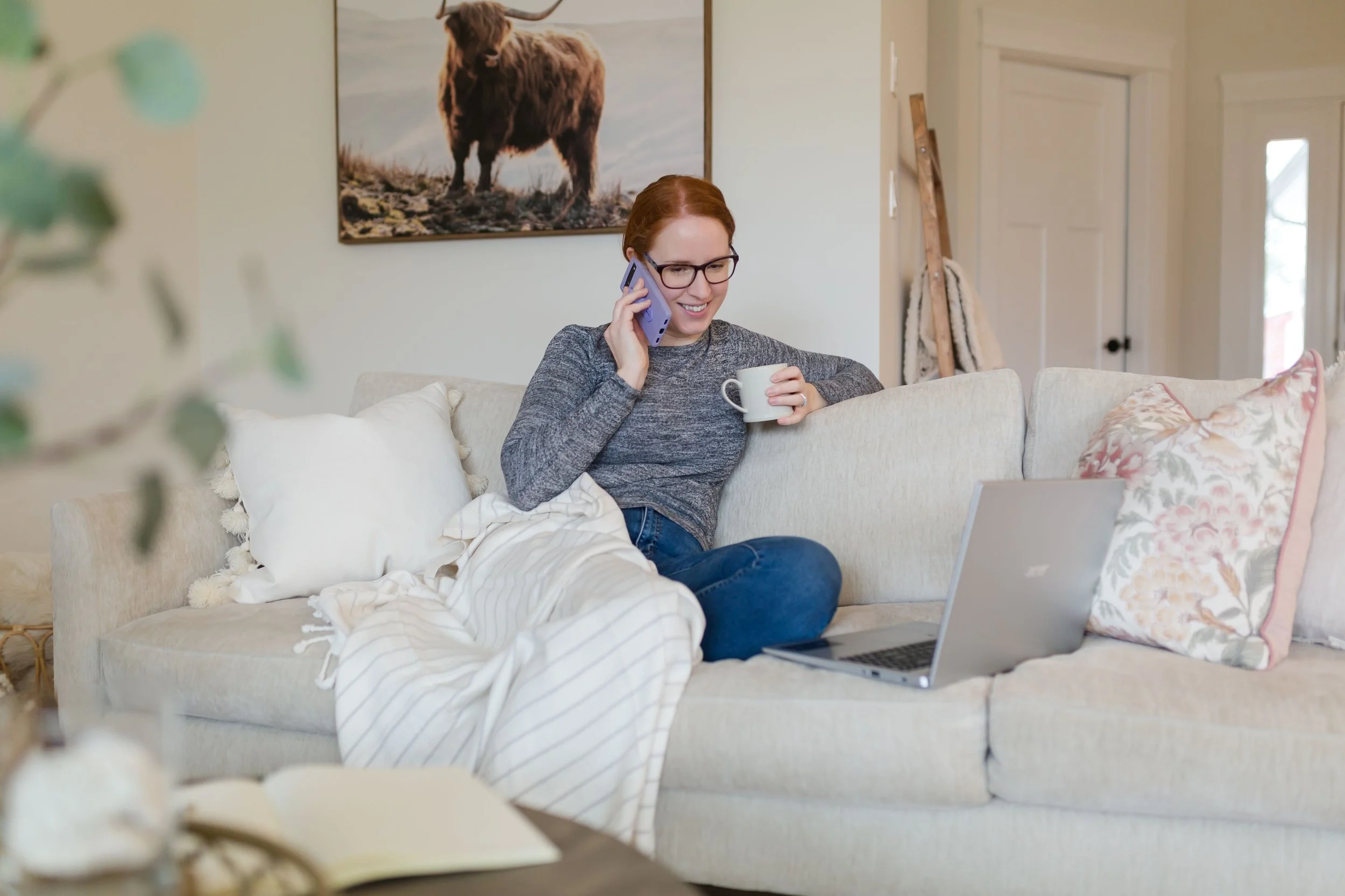 Katie Eberman of Simply by Katie, an Edmonton website designer, sitting on a couch with coffee and a laptop while helping a client build their next-level Squarespace personal brand.