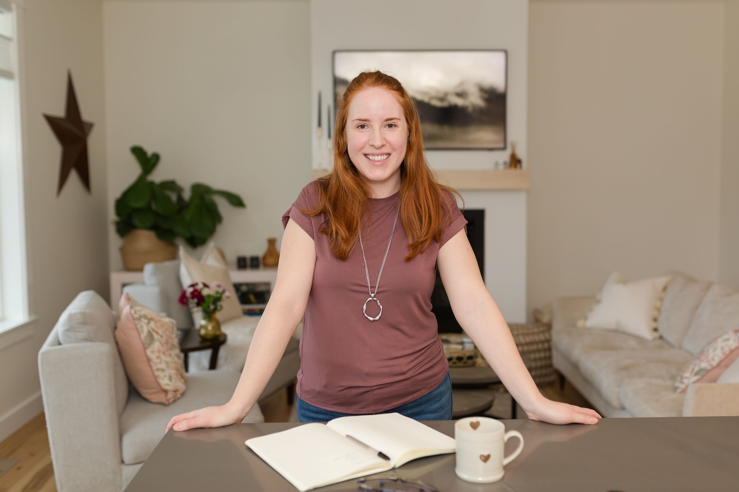 Katie Eberman, female web designer and website copywriter for female entrepreneurs, smiling in front of a fireplace on her About page
