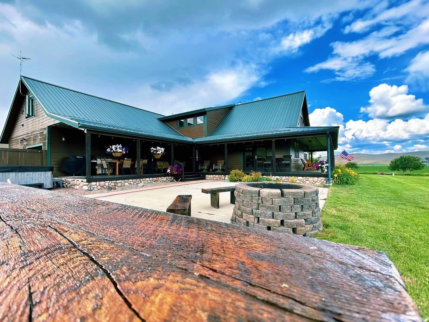 A modern house with a blue metal roof and a large covered porch, surrounded by a green lawn and wide open sky with clouds.