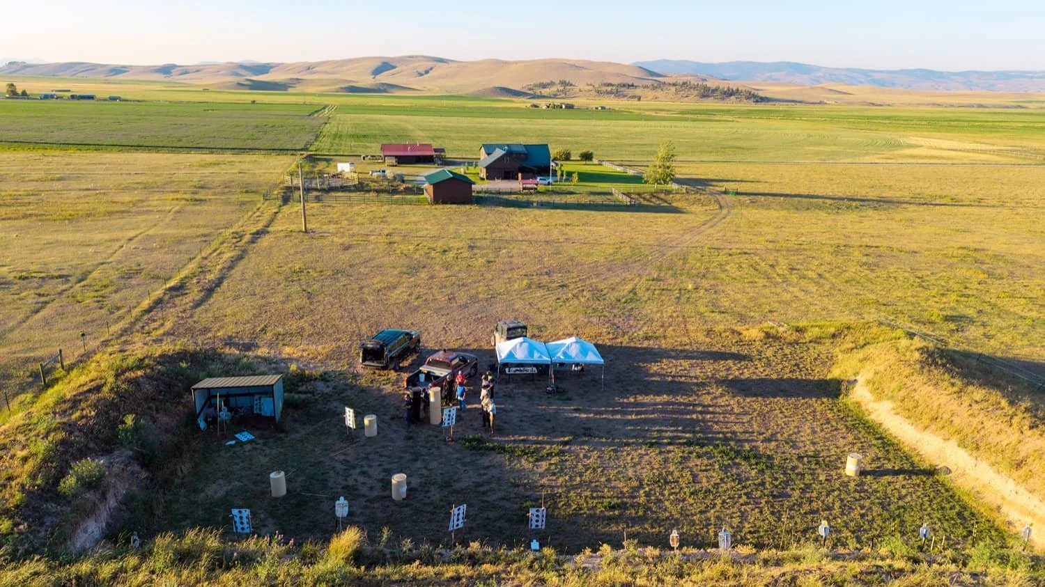 An outdoor shooting range in a rural area with targets set up and people practicing shooting.