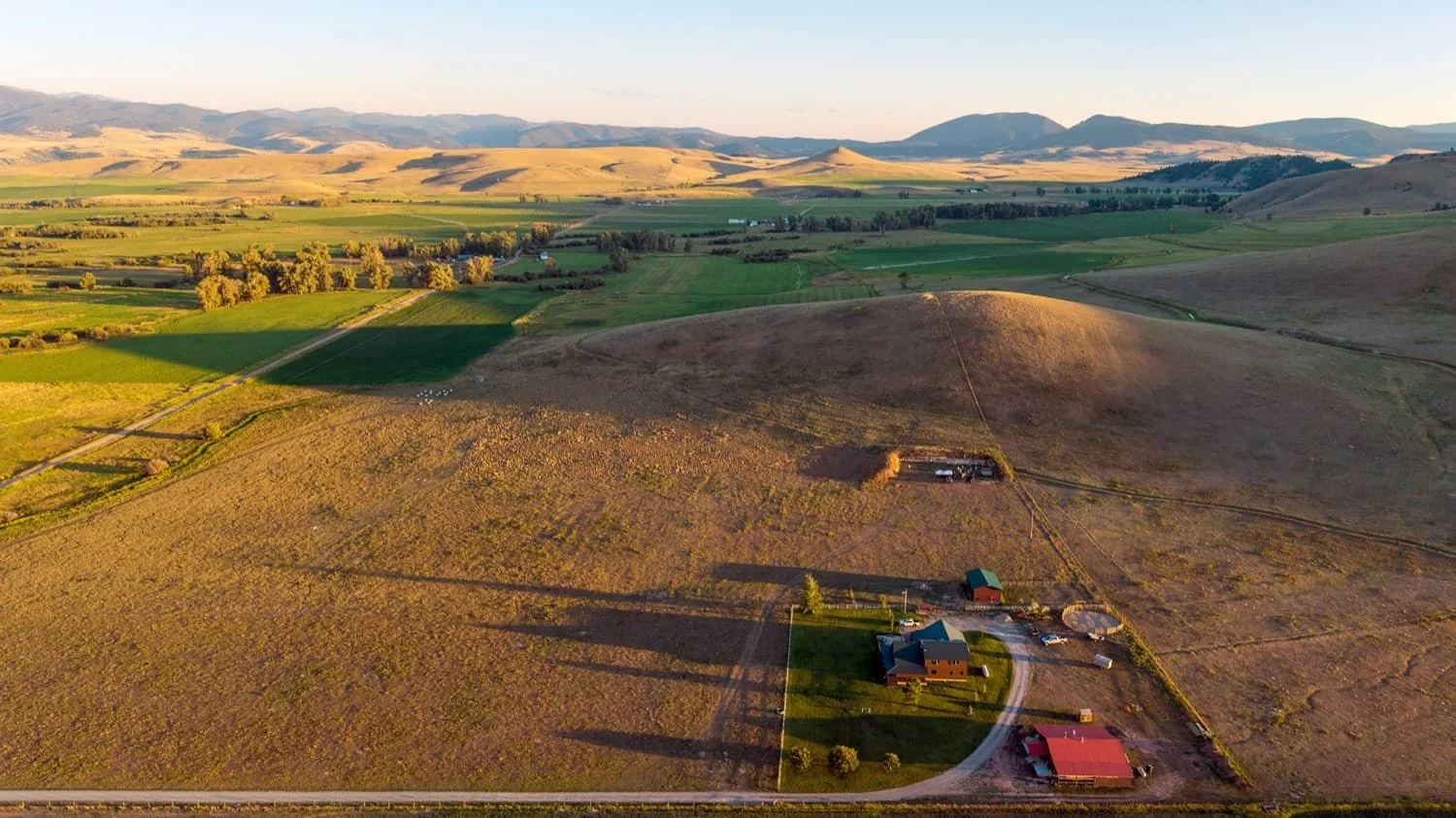 Aerial view of a rural landscape with rolling hills, green fields, and a farm with houses, barns, and a circular driveway.