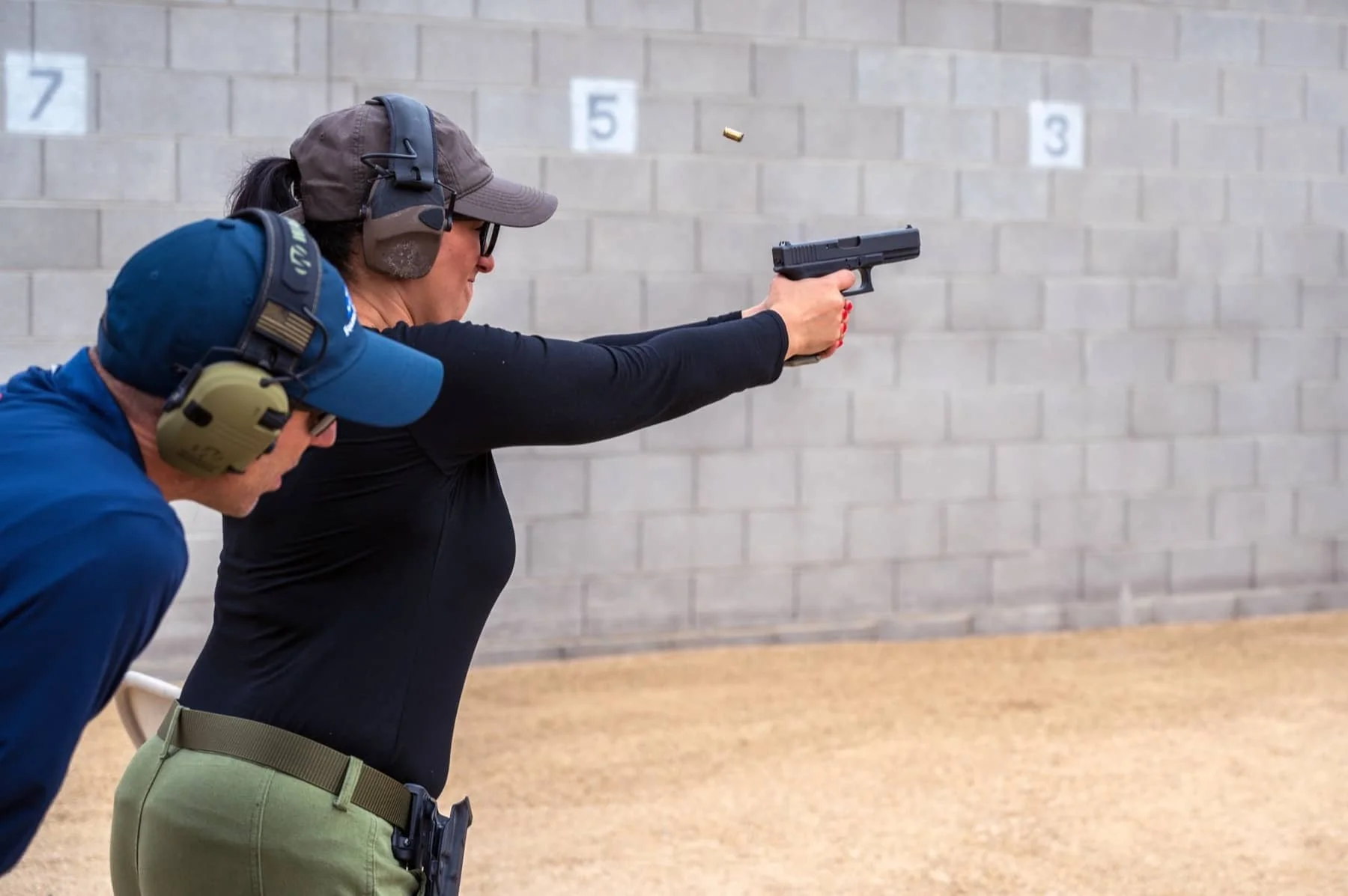 A woman firing a handgun at a shooting range with two people watching in the background.