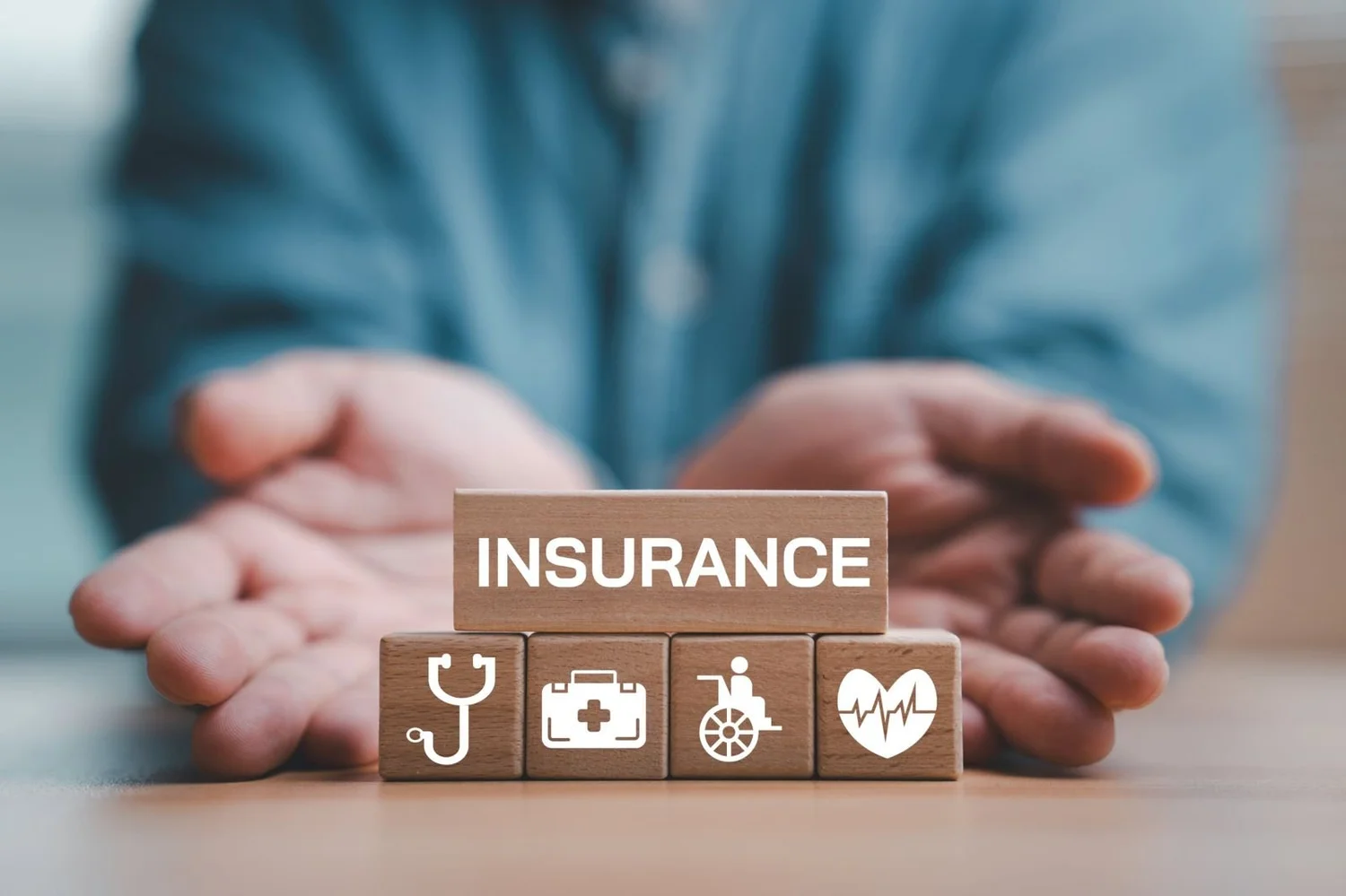Hands around wooden blocks spelling insurance, with health and disability icons