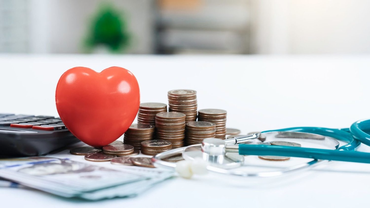 A red heart beside stacks of coins, a calculator and a stethoscope