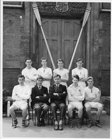 A black and white vintage school photograph of nine young men posed in two rows, wearing white sports kit, with two long oars crossed behind them, the kind of irreplaceable historical image SocialArchive is built to preserve.