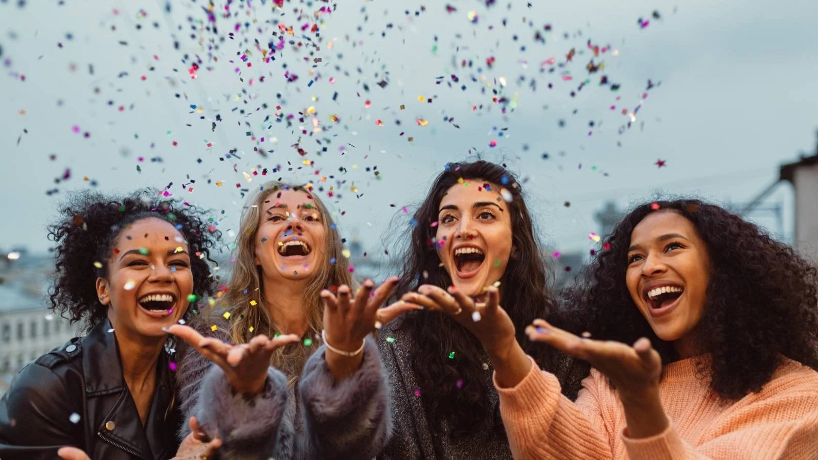 Four joyful young women laughing and throwing colourful confetti in the air, capturing the celebration and emotional connection that inspires alumni and donors to give back.