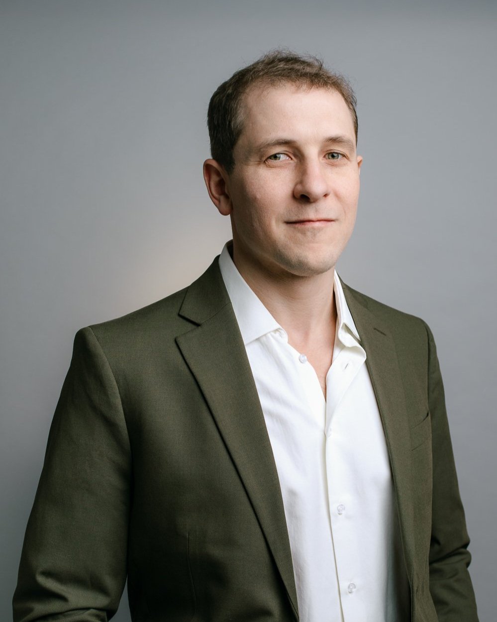 Headshot of Joel Loughead, Green Party of Ontario candidate for Bruce-Grey-Owen Sound, in front of a grey background, wearing a green suit with a soft, closed-mouth smile.