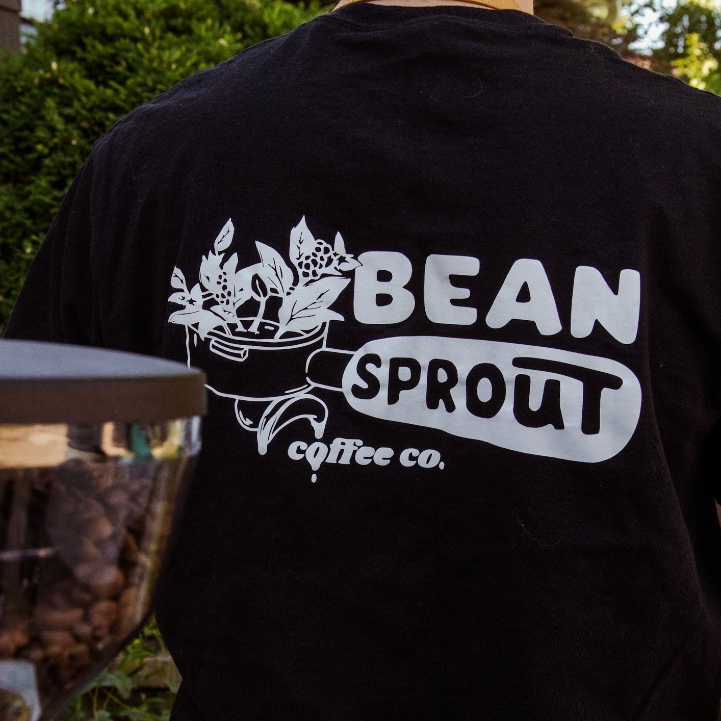 Back of person wearing a black shirt with 'Bean Sprout Coffee Co.' and plant graphic.