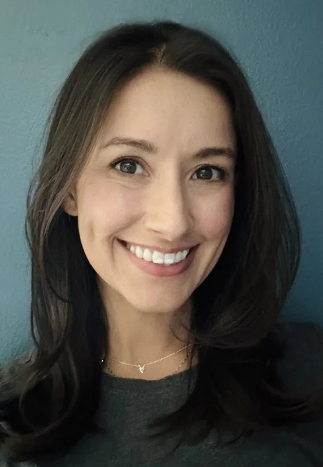 A female psychologist smiling in front of a blue wall.
