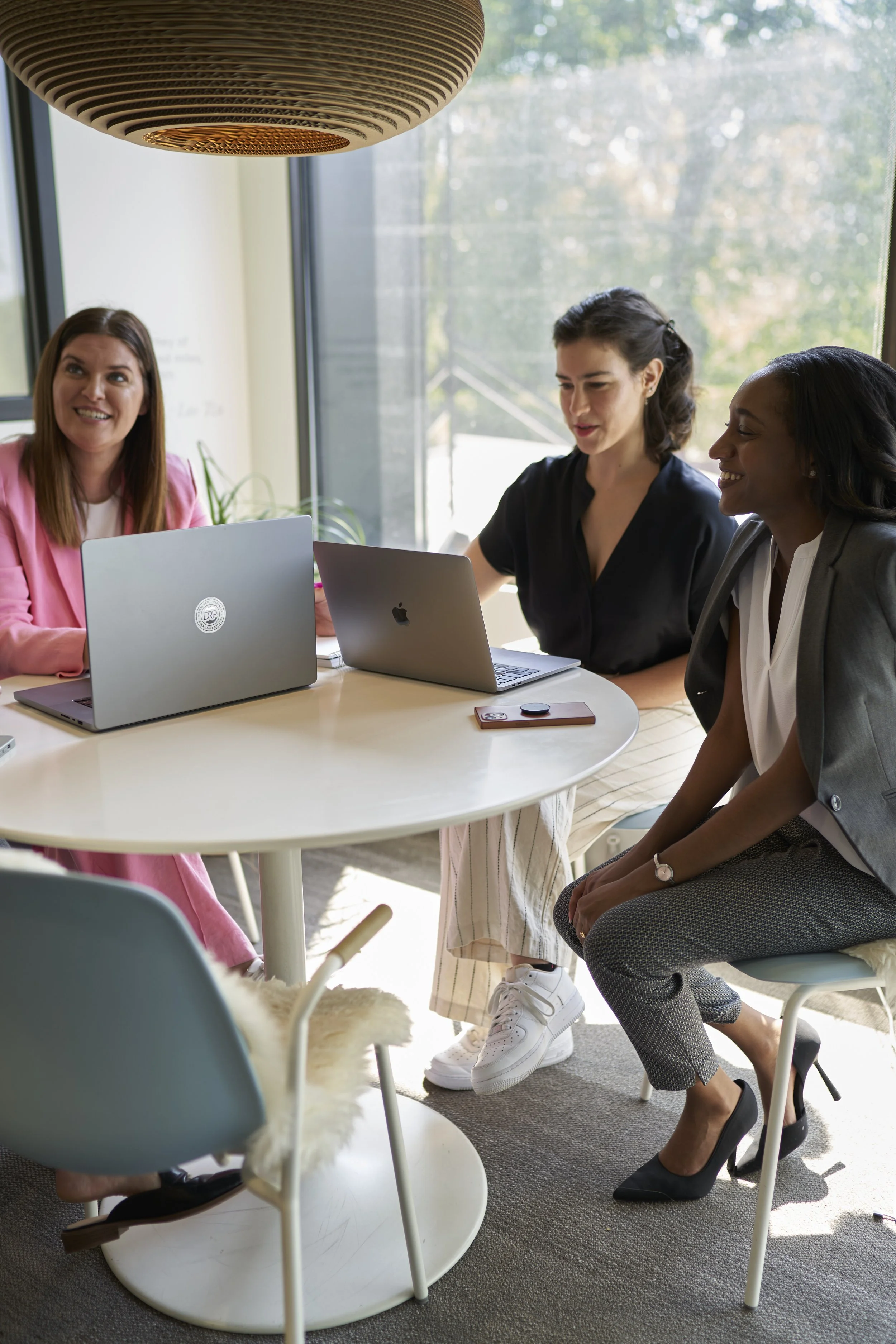 Three people sit at a table with their laptops open