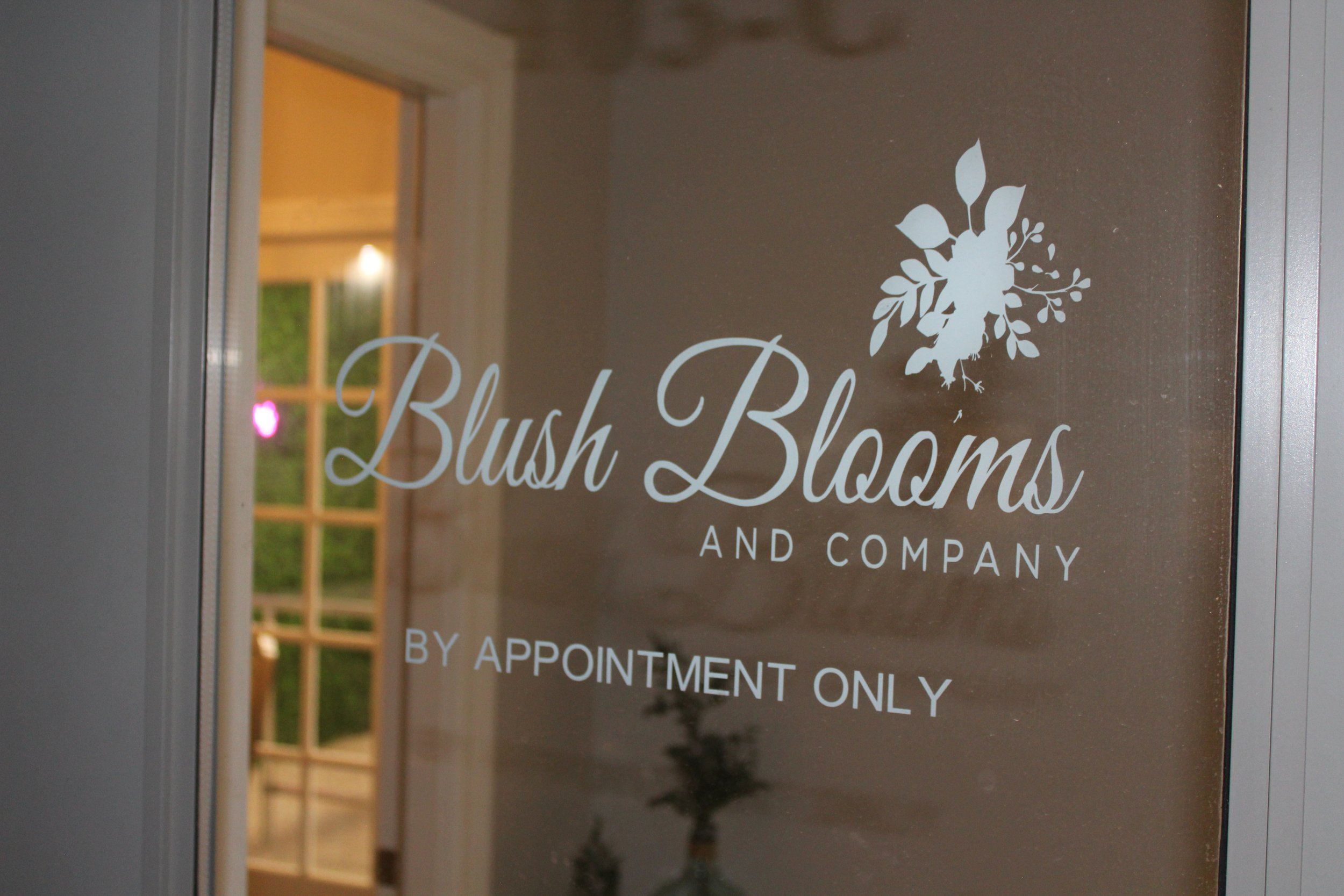 Glass door with "Blush Blooms and Company" text, floral logo, and "By Appointment Only"