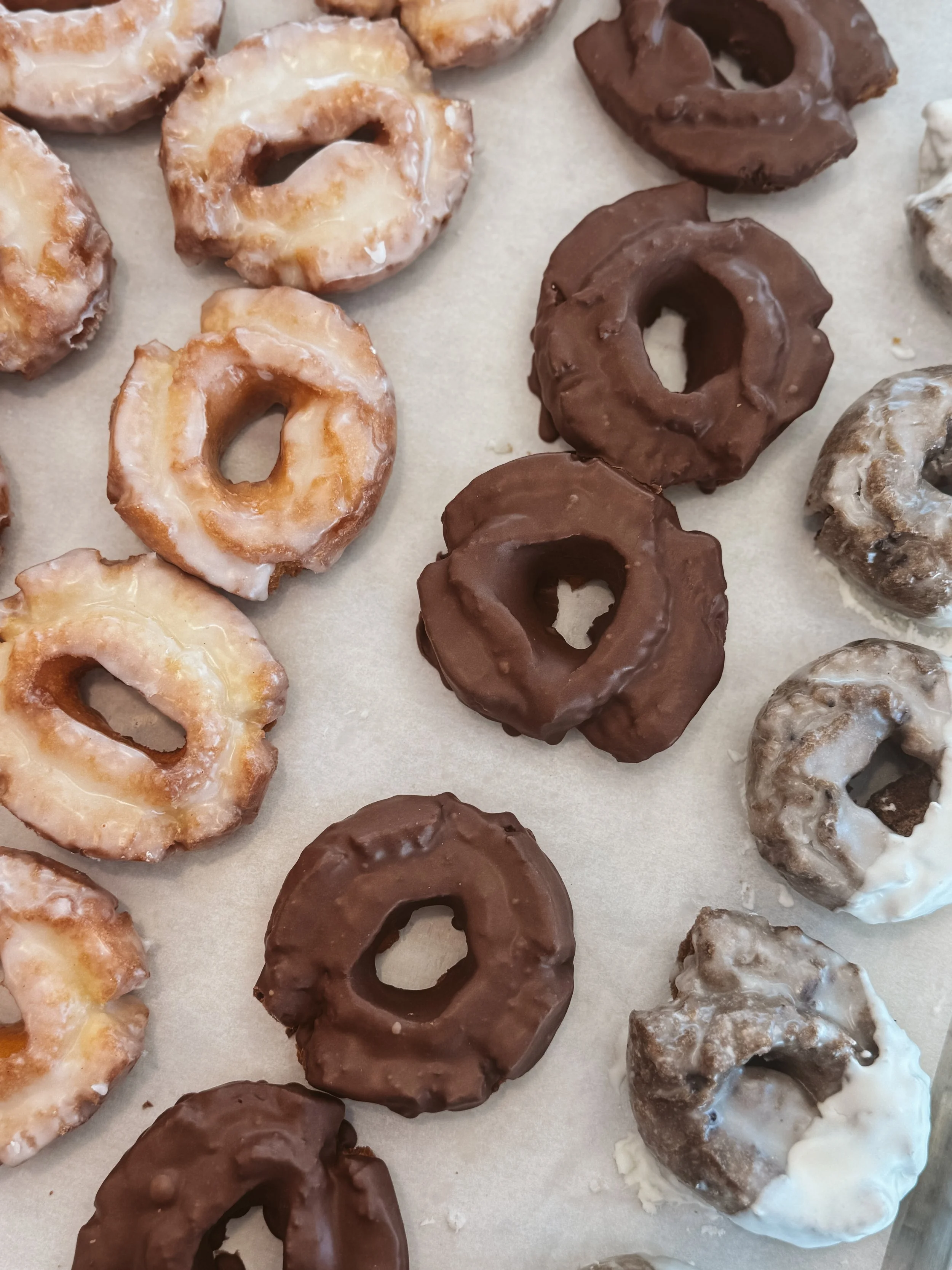 Assorted donuts with glazed, chocolate, and powdered toppings arranged on parchment paper.