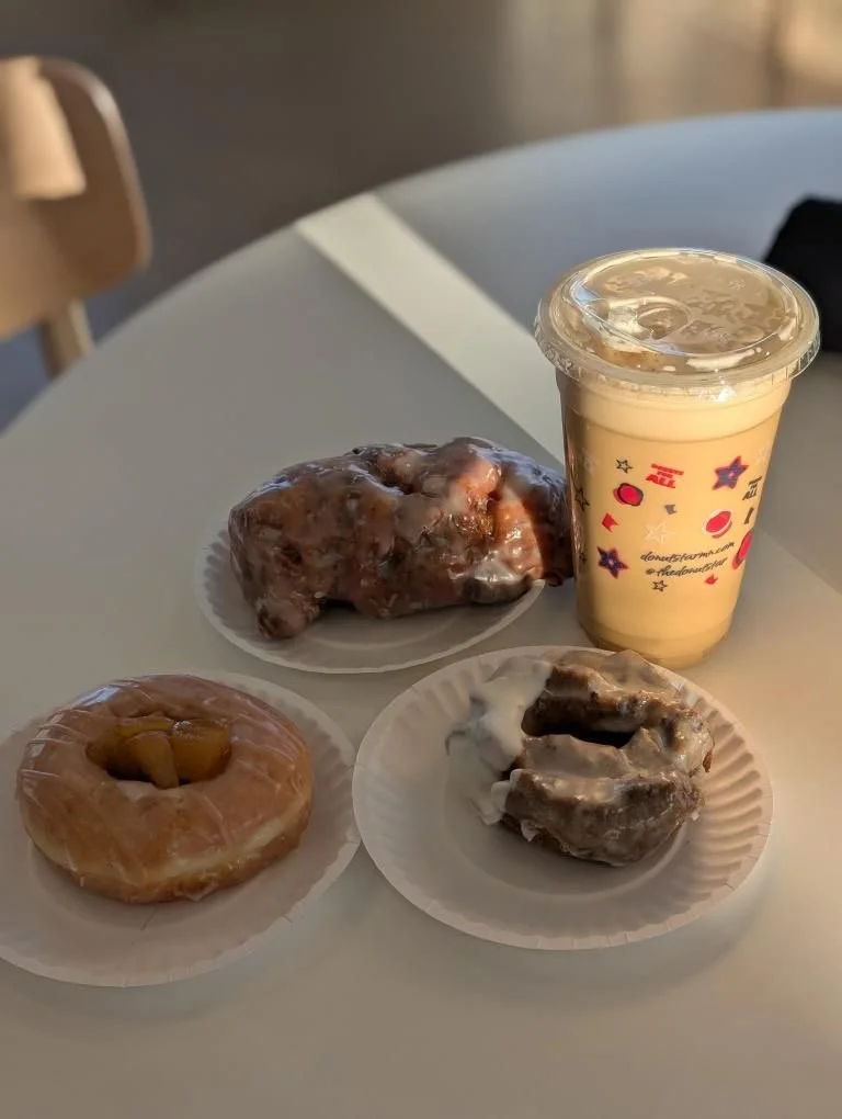 A table with a donut, a cinnamon roll, a glazed donut with caramel, and a cup of iced coffee.