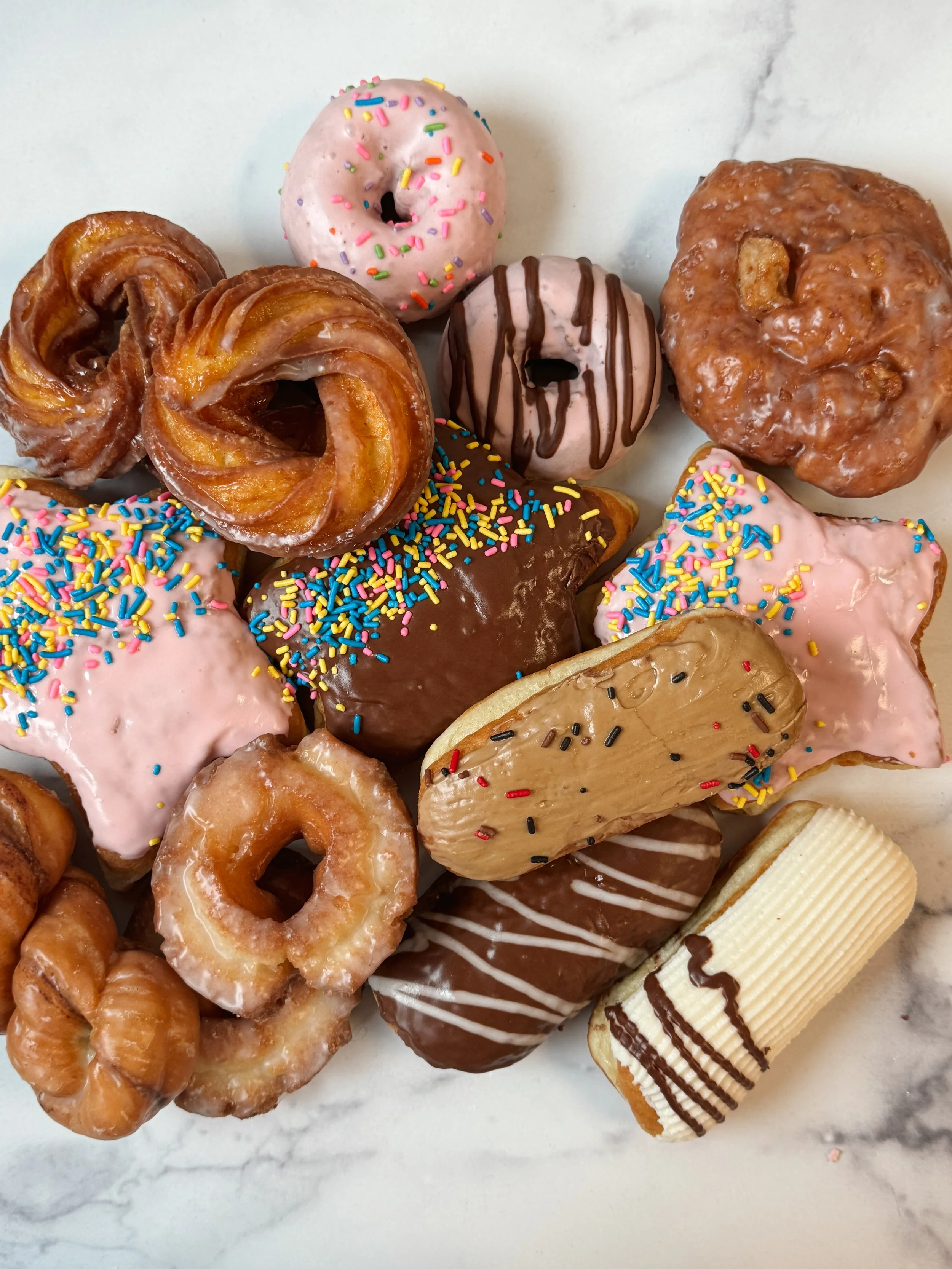 Assorted donuts with various toppings such as sprinkles, chocolate glaze, and icing on a marble surface.