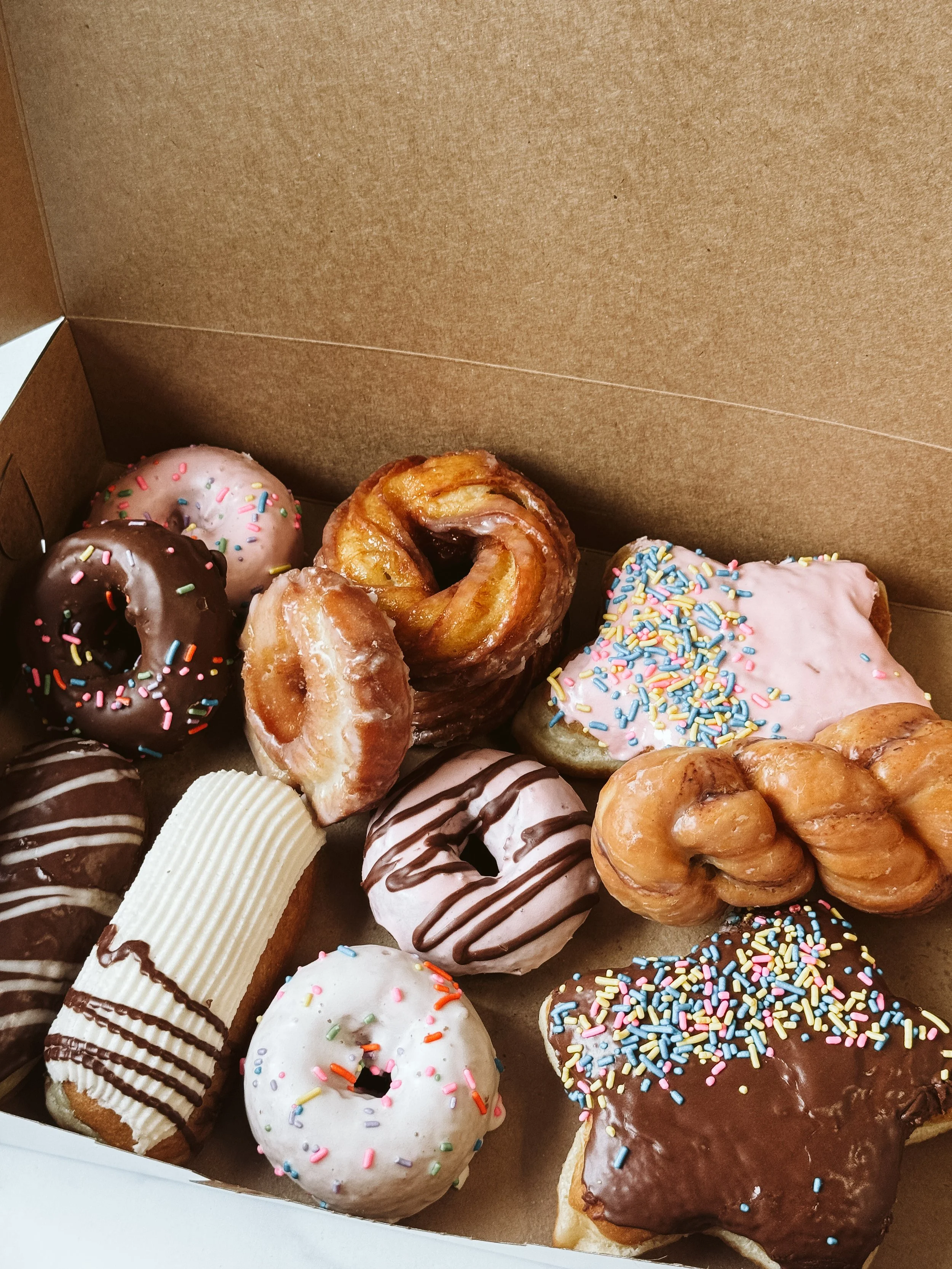 Assorted donuts with various frosting and sprinkles in a cardboard box.