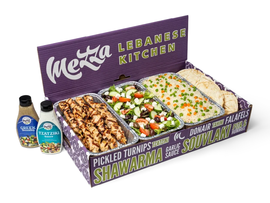 Mezza box filled with chicken souvlaki skewers, pita, salad, rice, with a bottle of dressing and tzatziki sauce beside the box.