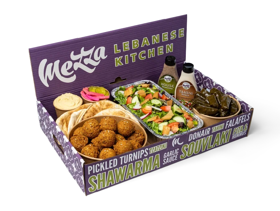 Mezza box filled with falafels, pita, salad, grape leaf rolls, a bottle of dressing and tahini sauce, and more.