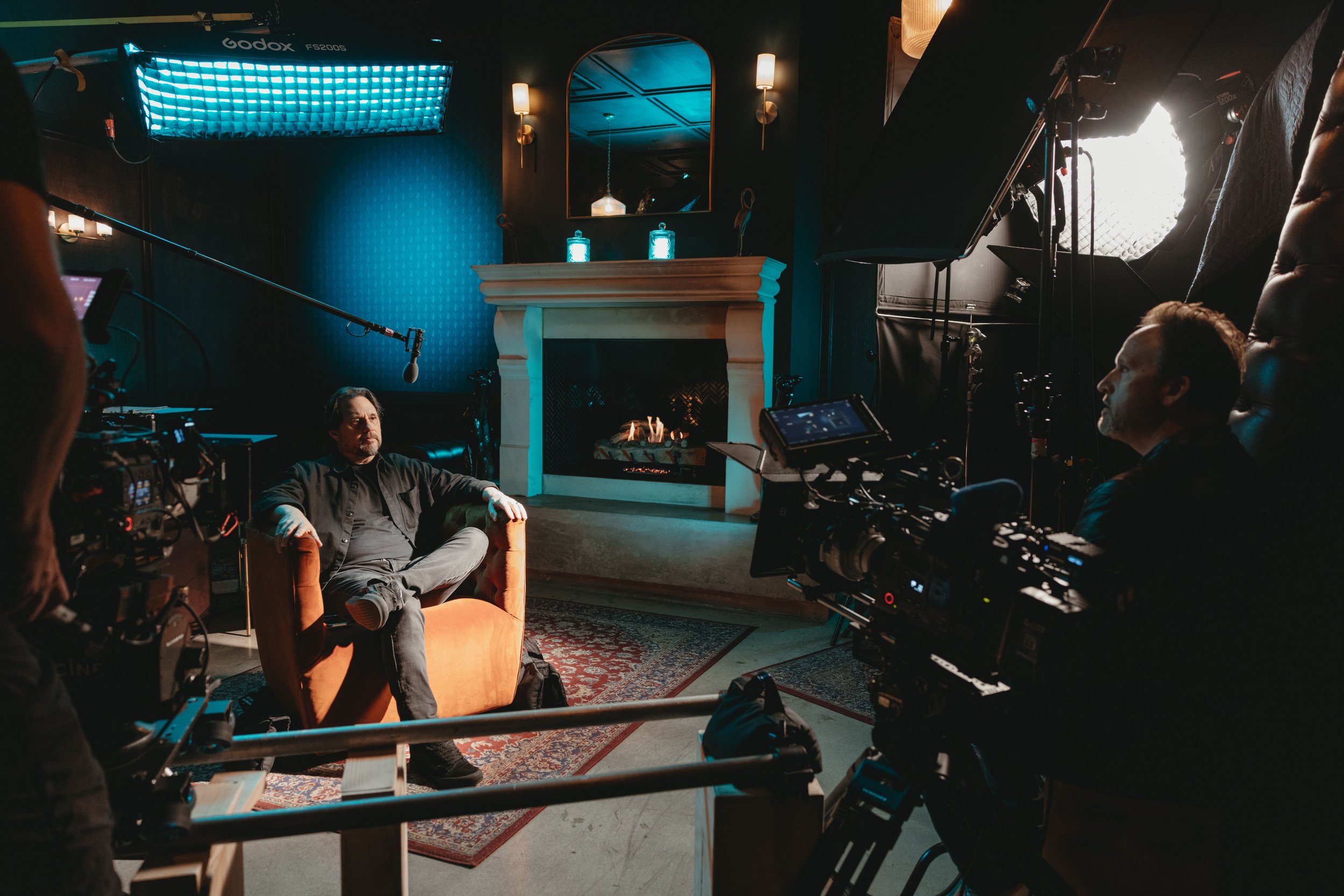 A talk at an event being recording while man sits in arm chair