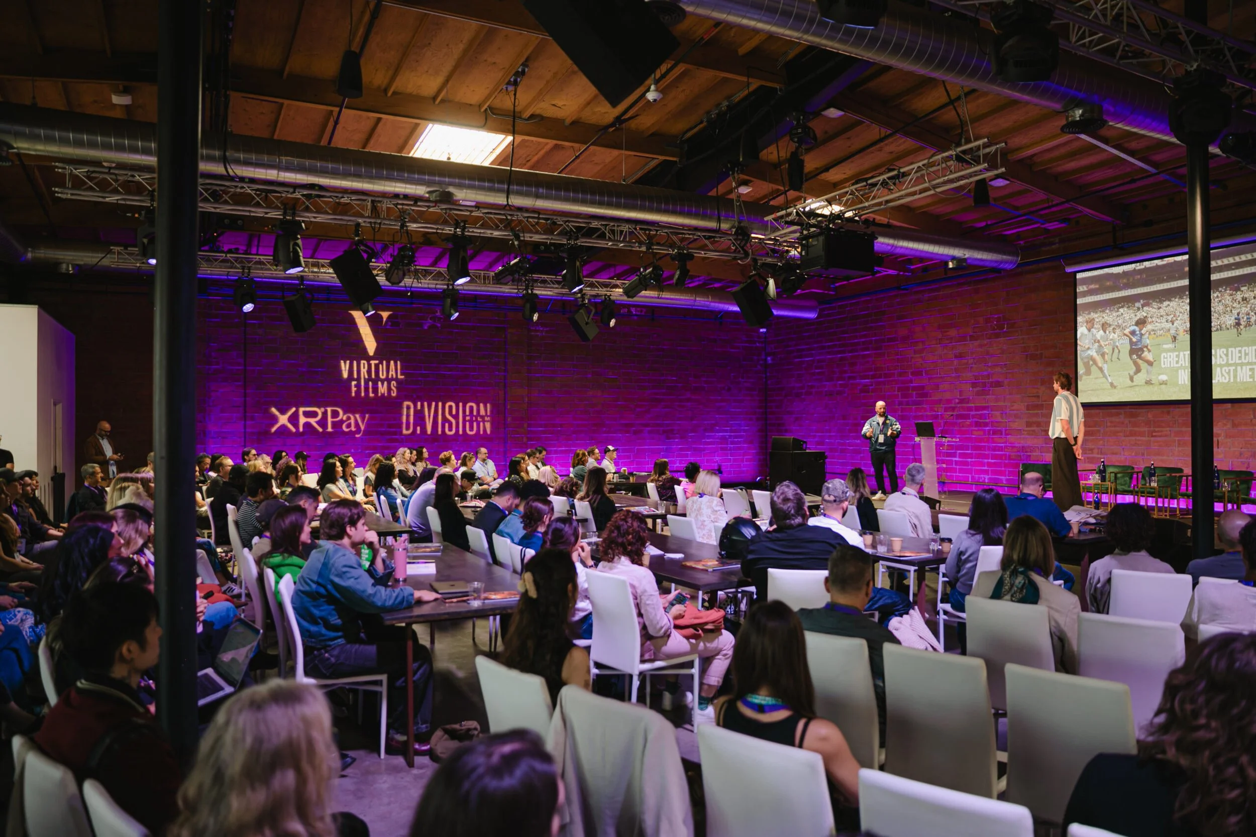 Seated guests listening to talk from the stage with purple lights during an event