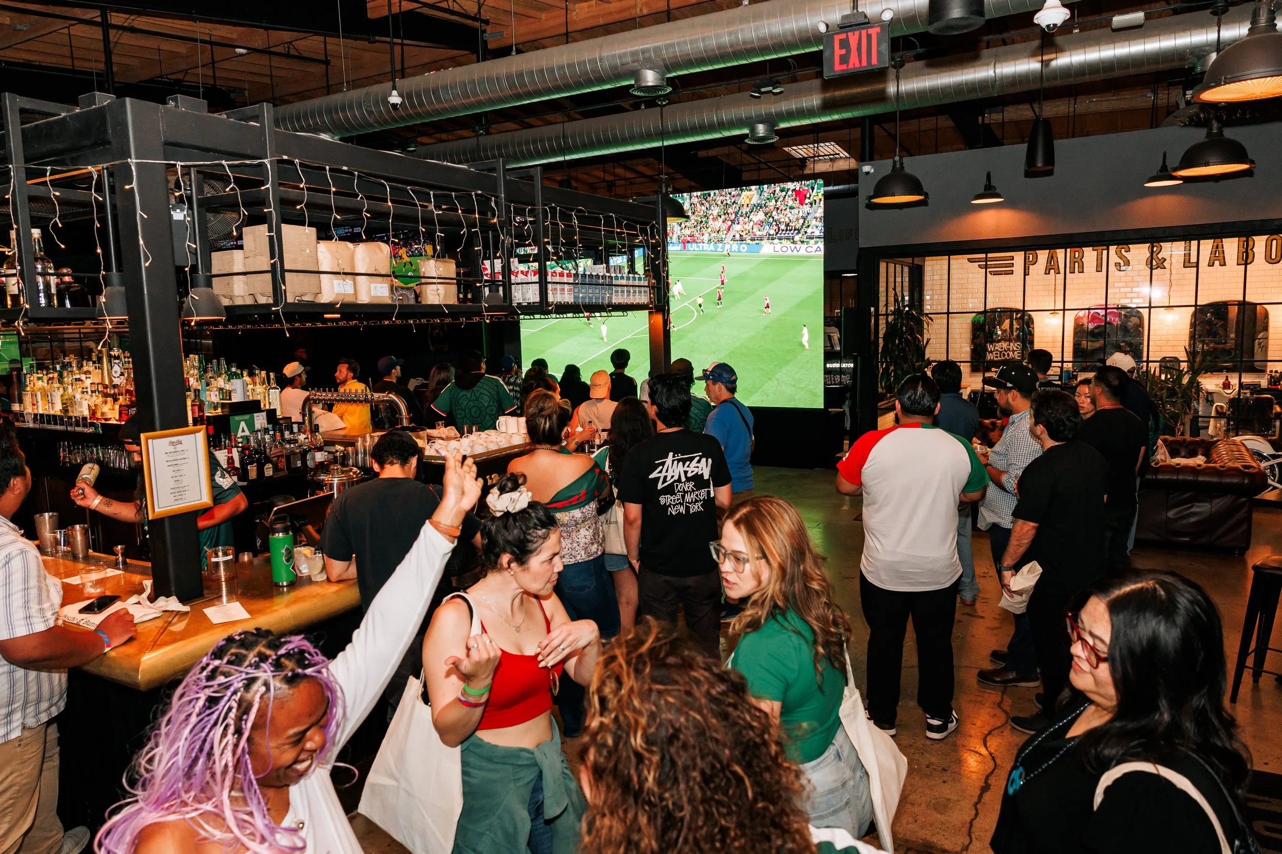 Dynamic scene of soccer fans chatting, drinking and watching two large projection screens during a watch party event