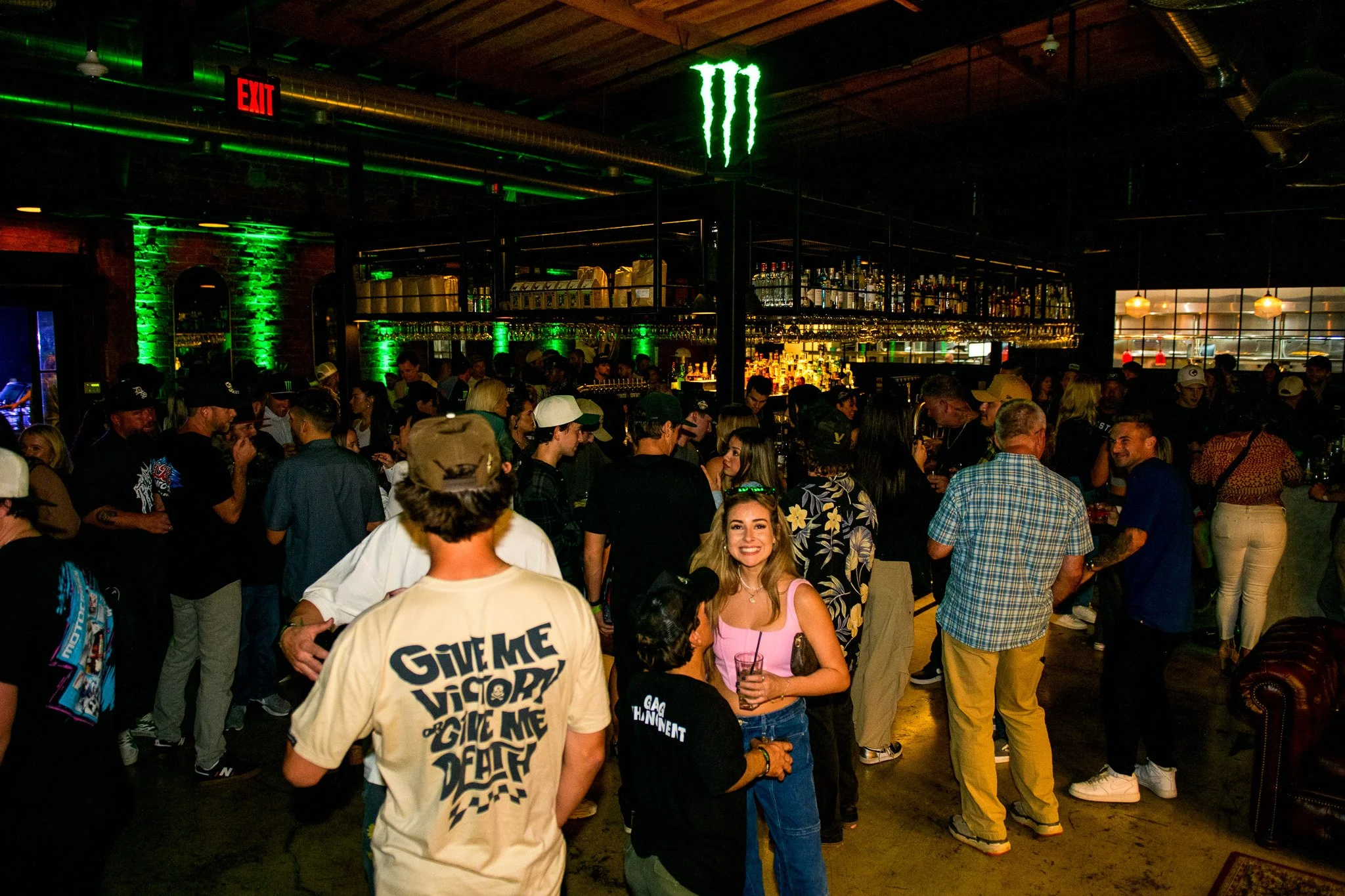 Dimly lit party scene and people smiling and drinking at an event at Bike Shed Moto LA