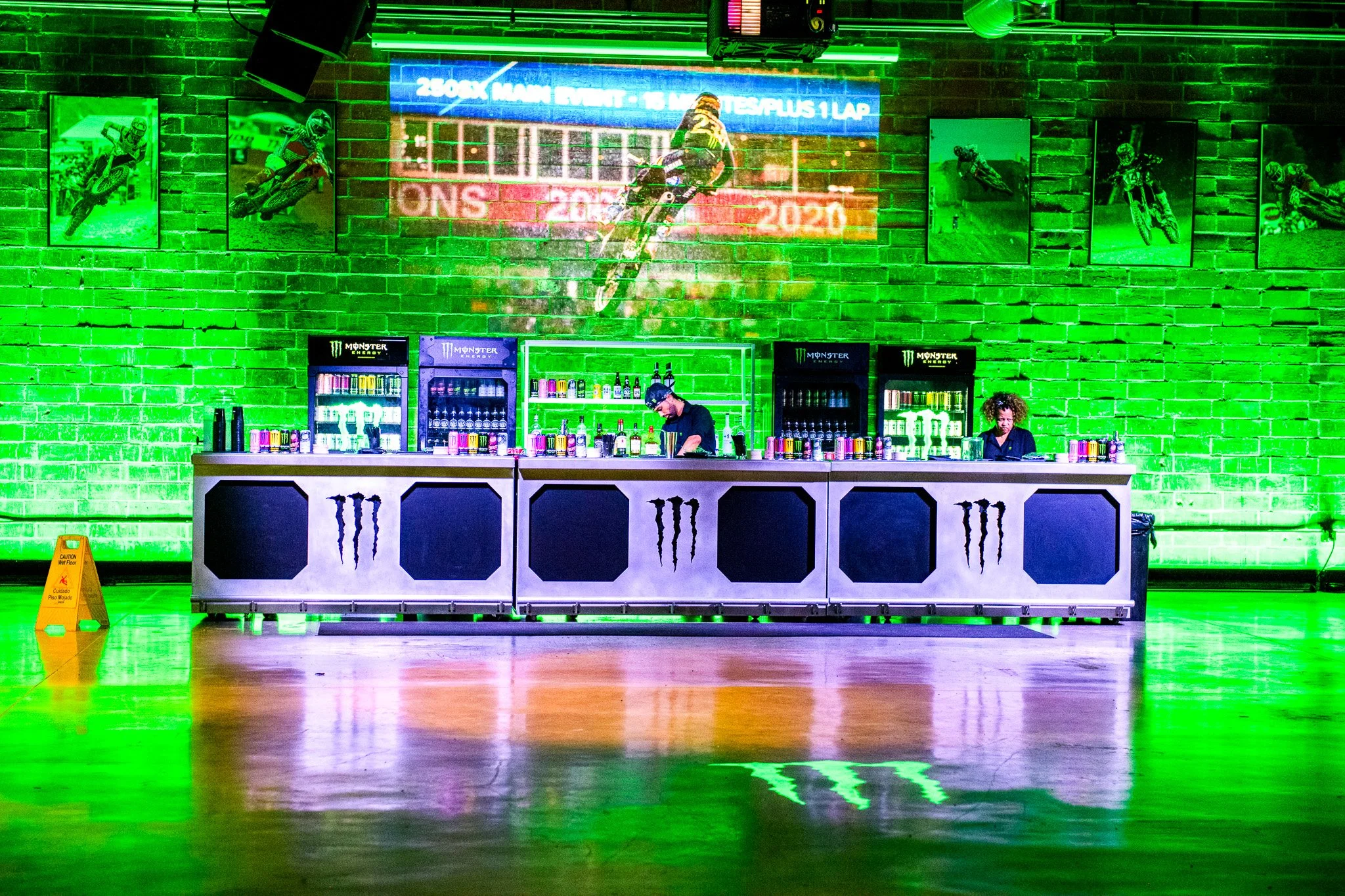 Huge Monster energy bar bathed in green lighting and artwork of motorcycle hung on the wall behind