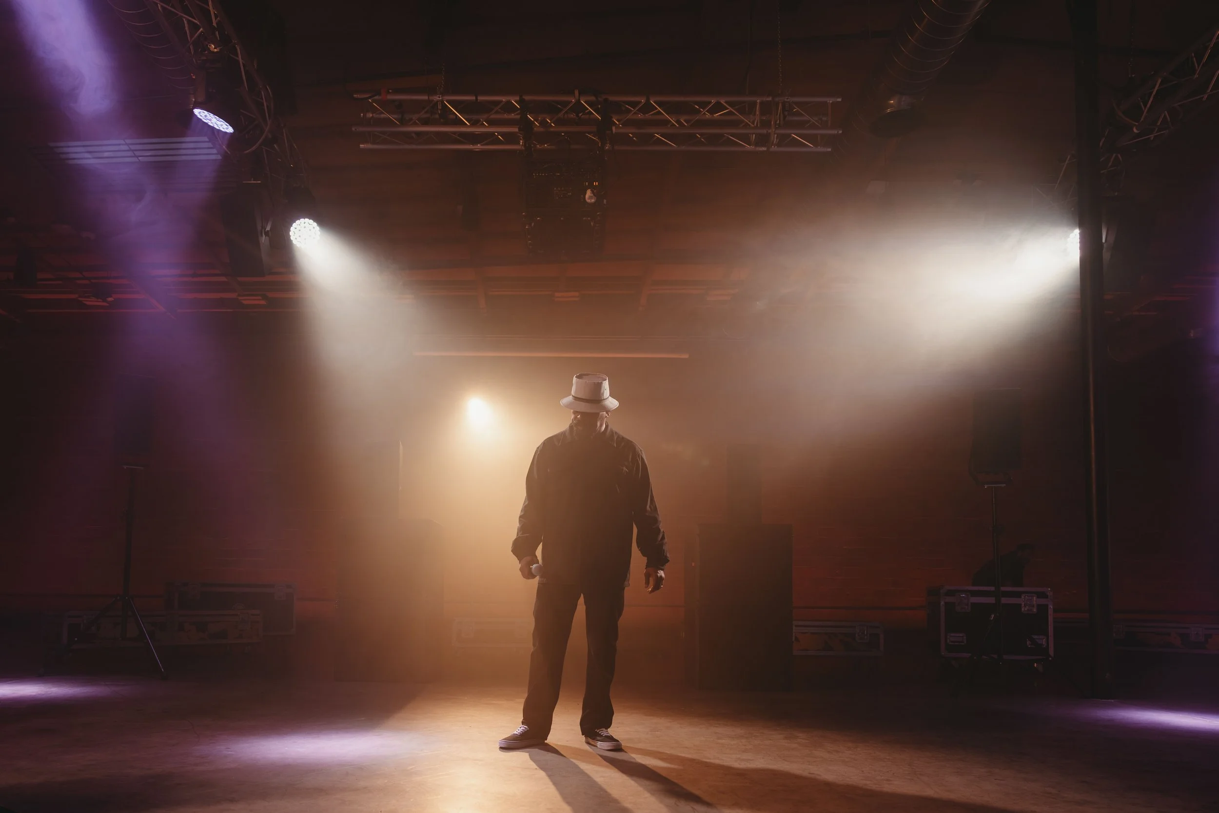 Lone man with trilby hat standing in a moody lit event space with a smoky haze in the air 