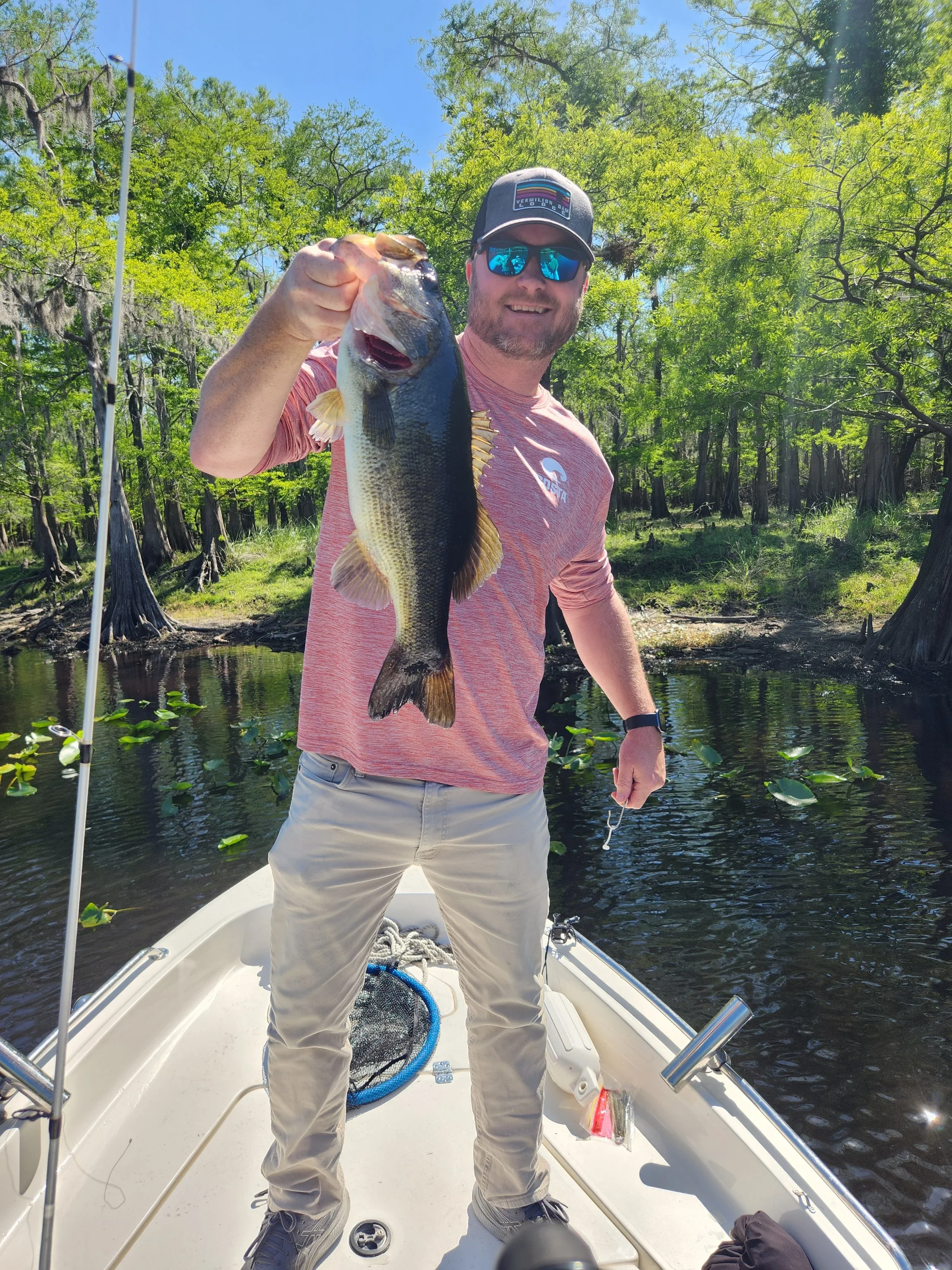 A man standing on a boat holding a large mouth bass on a  river fishing charter