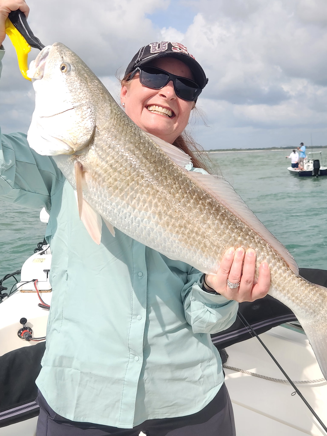 Woman holding a large bull red on a boat with water and other boats in the background.