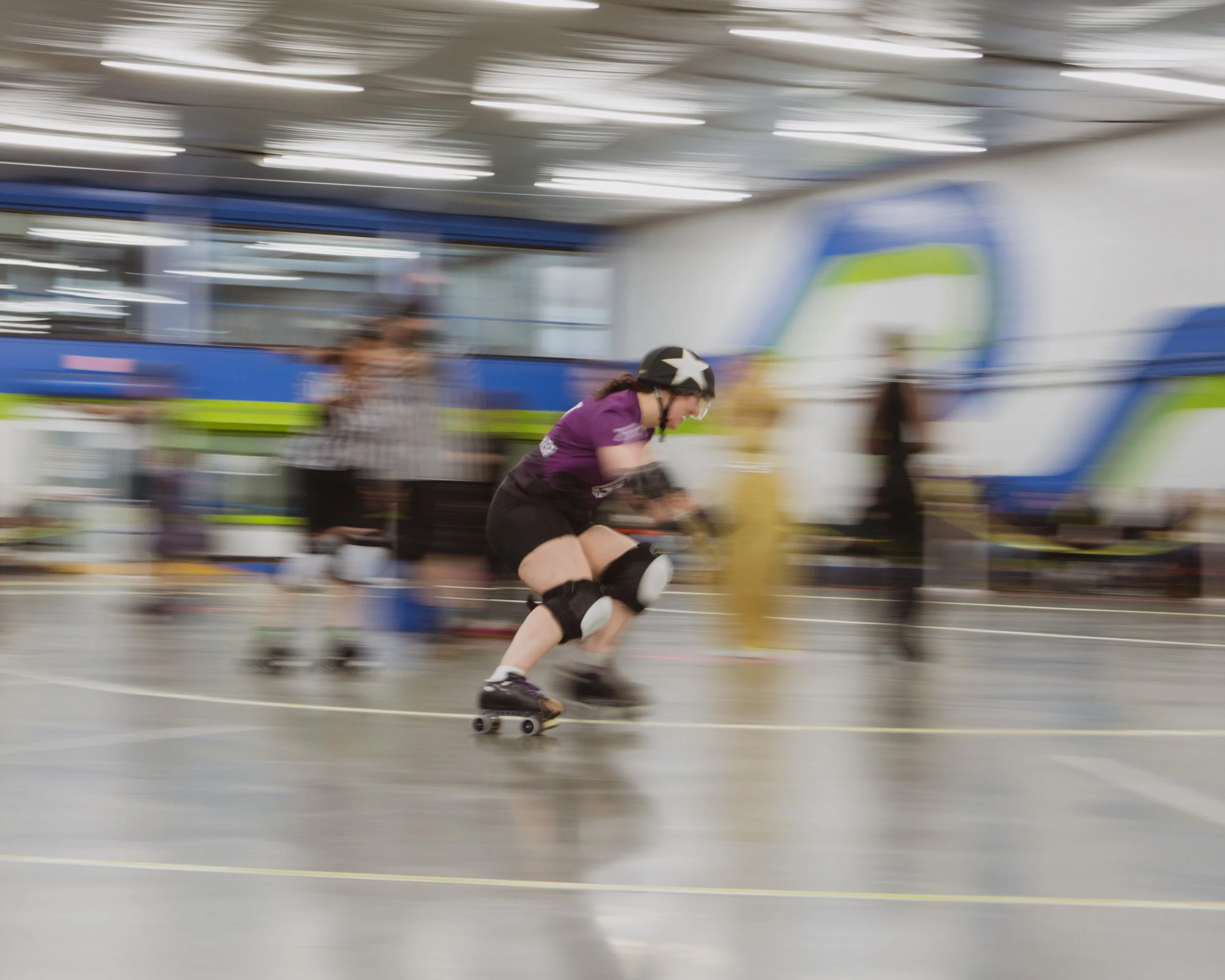 A focused jammer skates around the oval track while motion blurs around them in a creative shutter drag shot taken in Victoria BC.