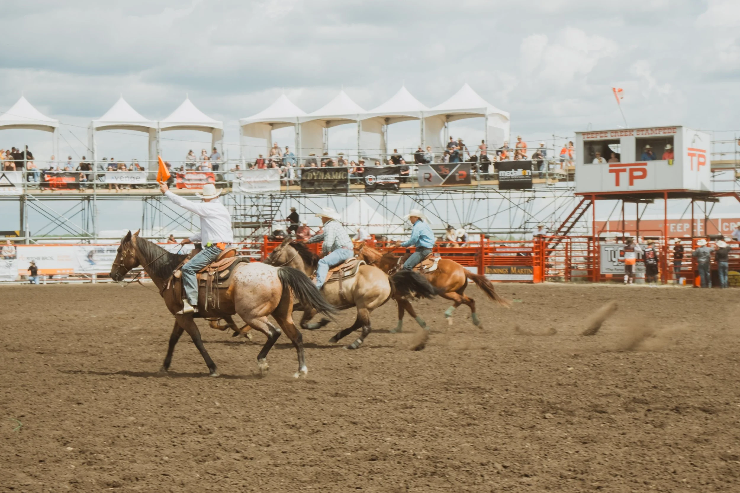 Three horses carrying riders race across the rodeo arena during the Teepee Creek Stampede.