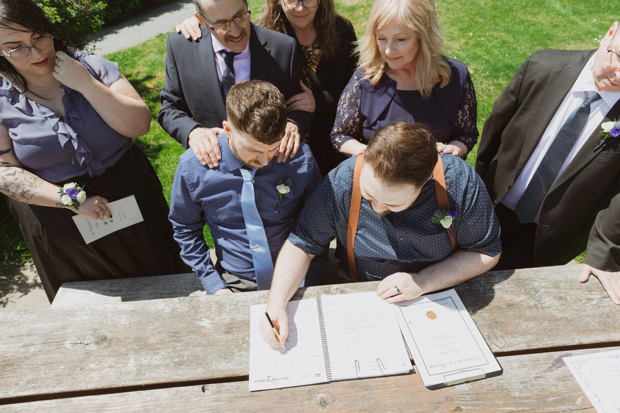 The two grooms sign their marriage licence surrounded by parents and their best friend during an intimate Victoria, BC elopement