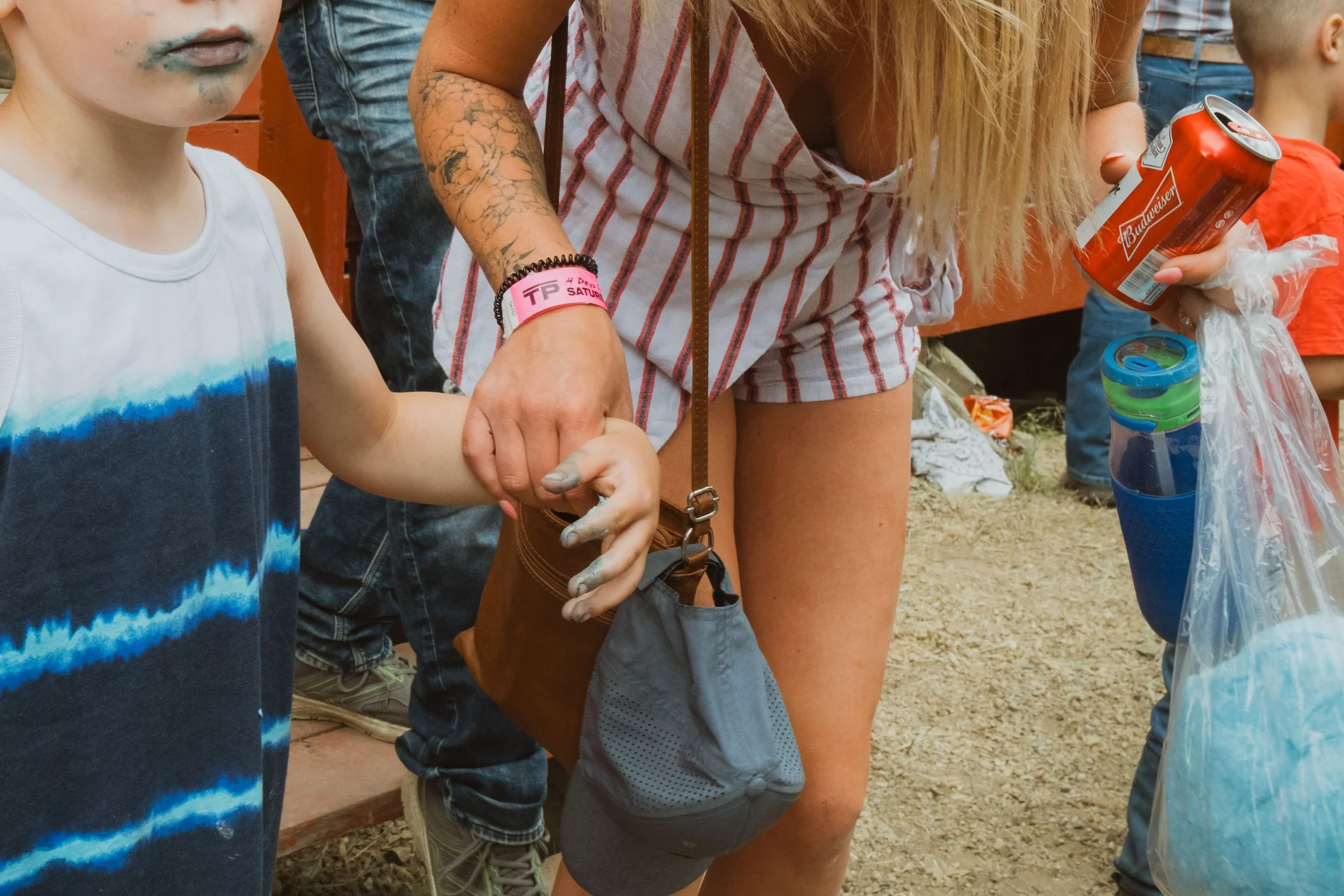 A close-up detail of a child with blue-stained hands and mouth while holding cotton candy beside a parent at the Teepee Creek Stampede.