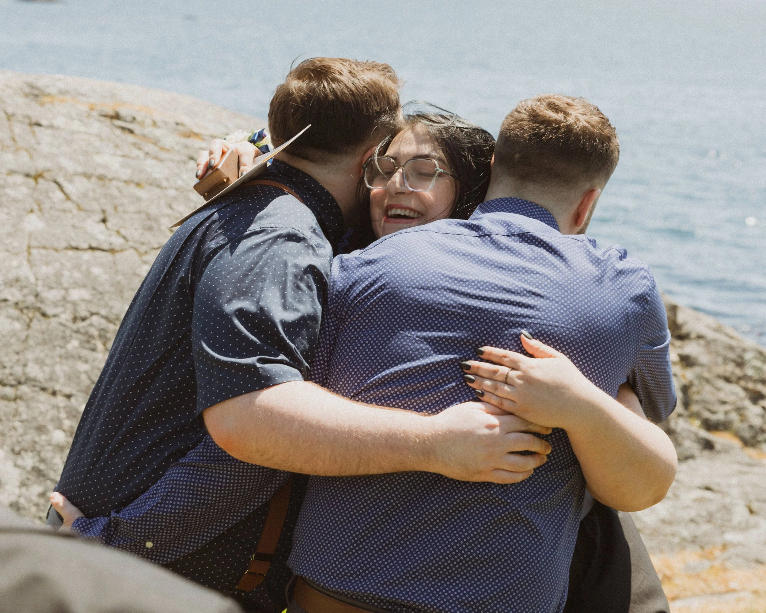 The two grooms hug their best friend together after she gives a reading during their elopement ceremony in Victoria, BC.